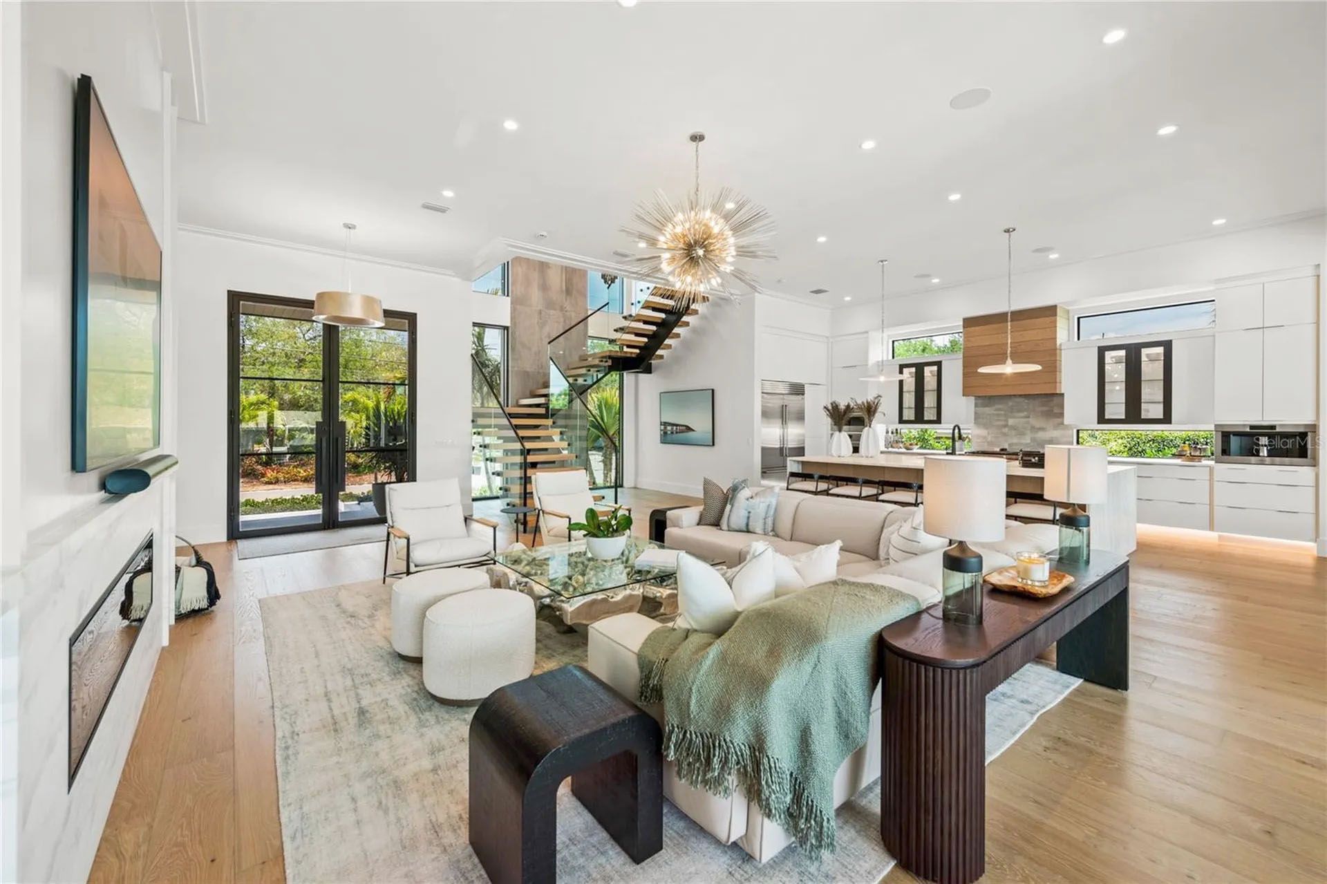 Bright open-concept living room and kitchen with white decor, wood floors, large windows, and a black dining table