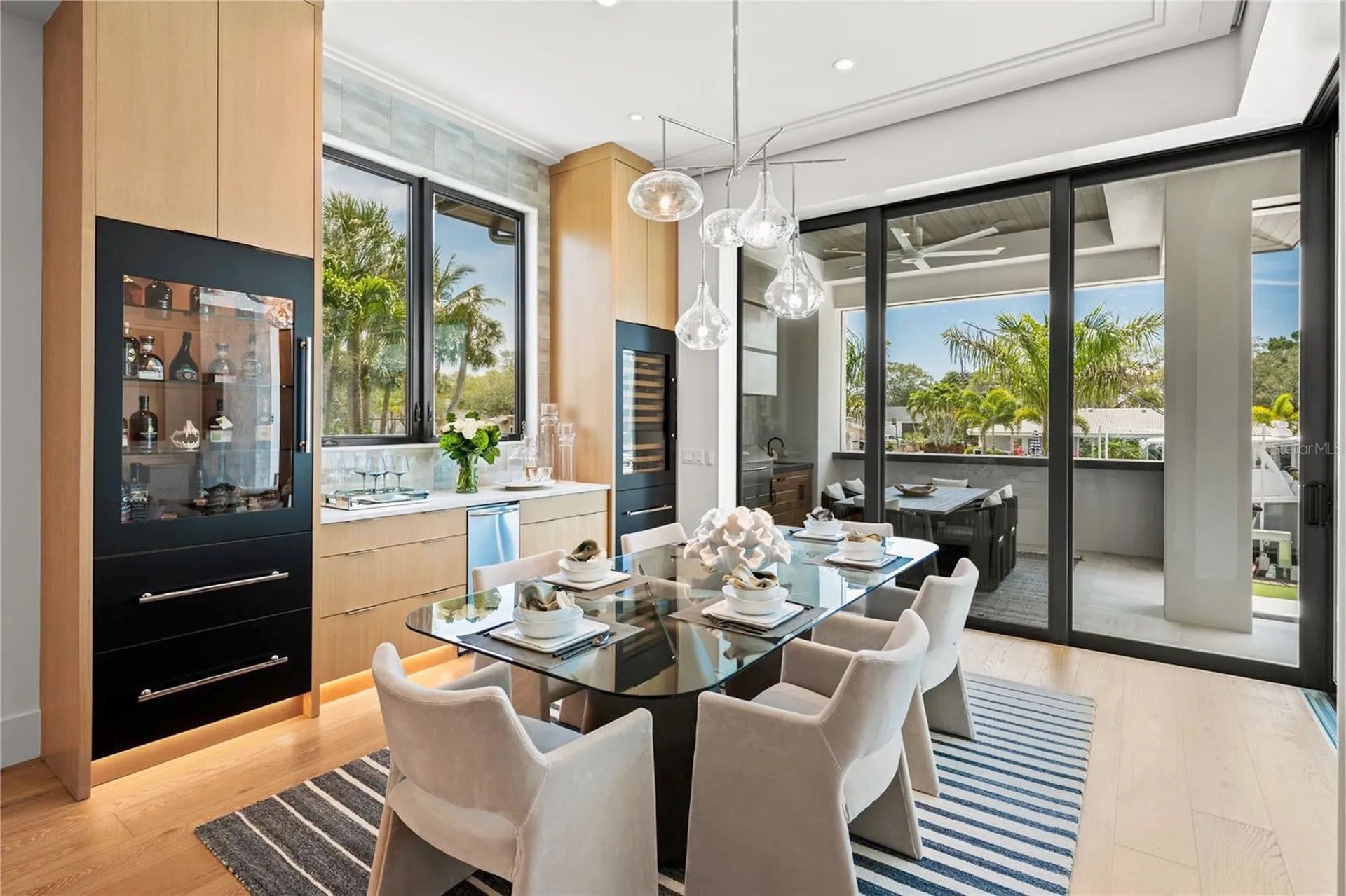 Bright modern dining room with glass table, beige chairs, wood cabinets, and balcony doors