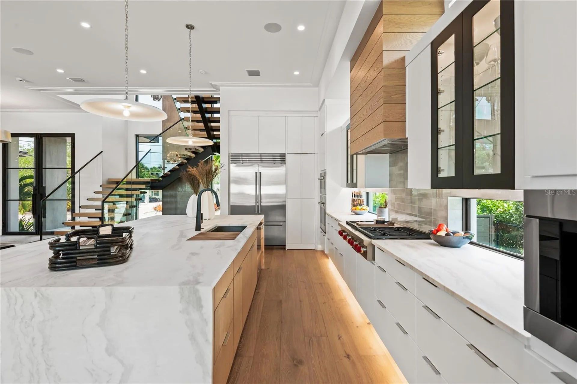 Modern kitchen with marble island, wood floors, white cabinets, and staircase