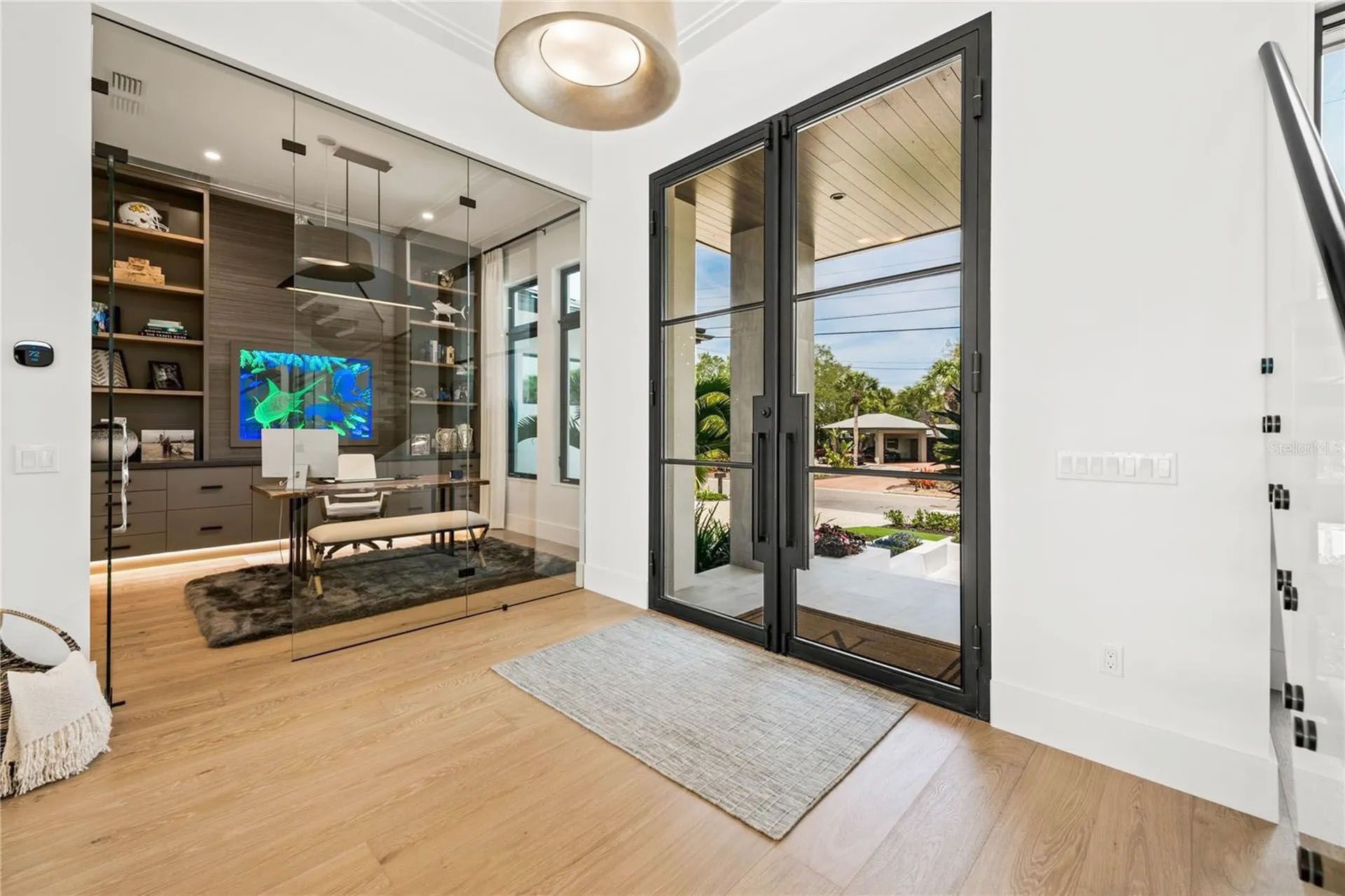 Modern living room with glass doors, wood floors, and a TV wall leading to an outdoor patio