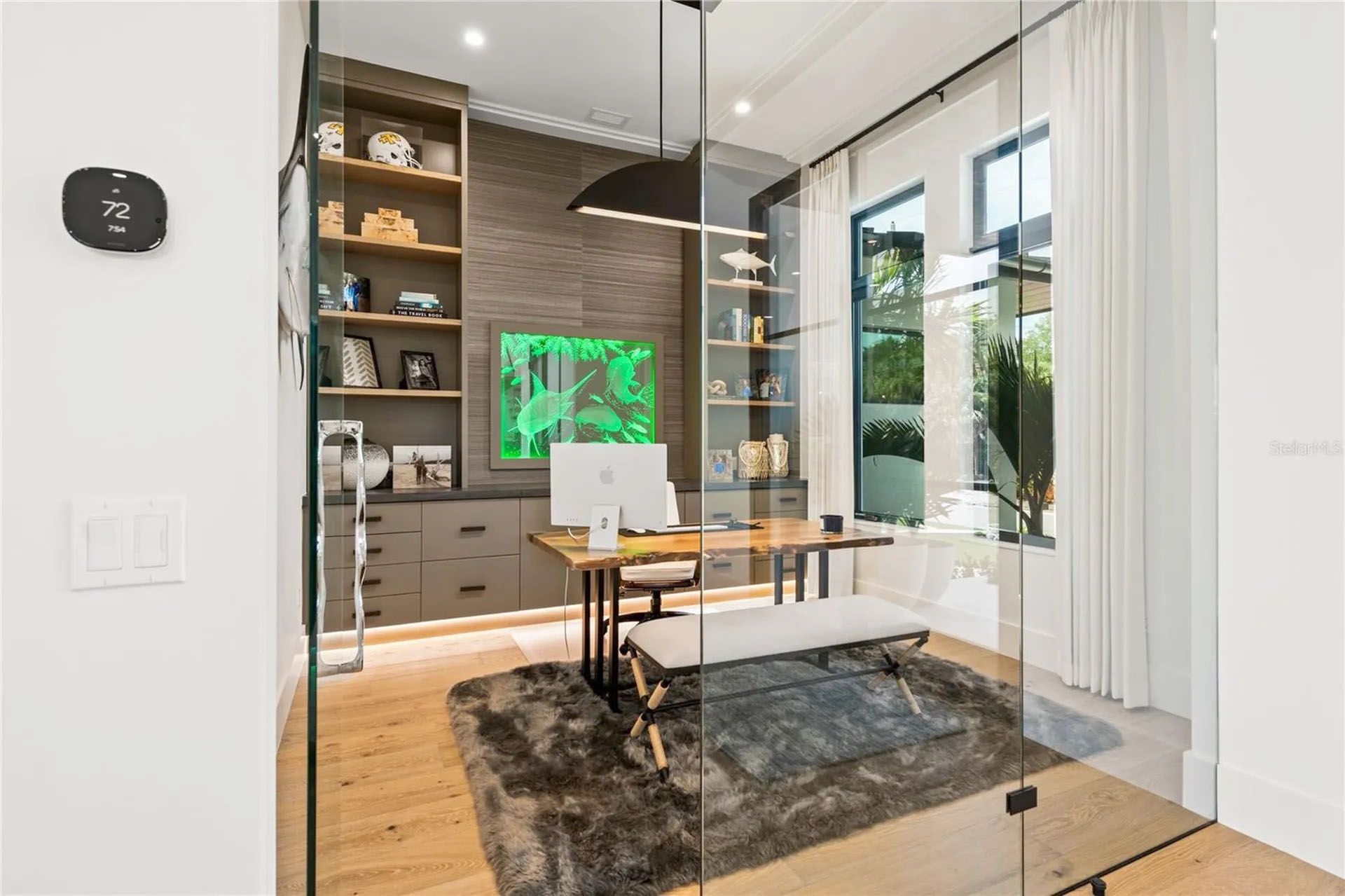 Modern home office with a desk, built-in shelves, large windows, and a gray rug in a bright room