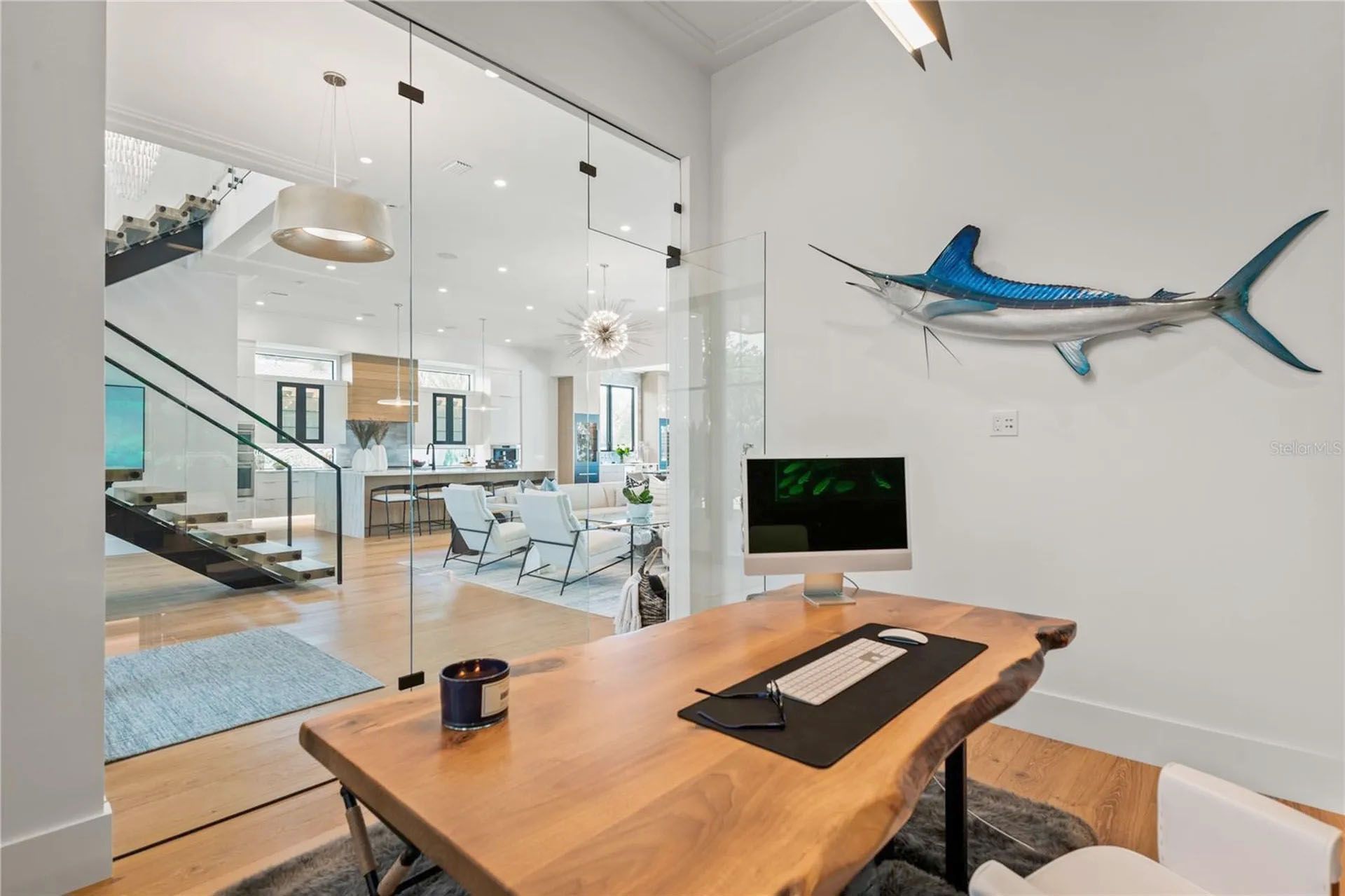 Modern home office with a wooden desk, glass walls, and staircase