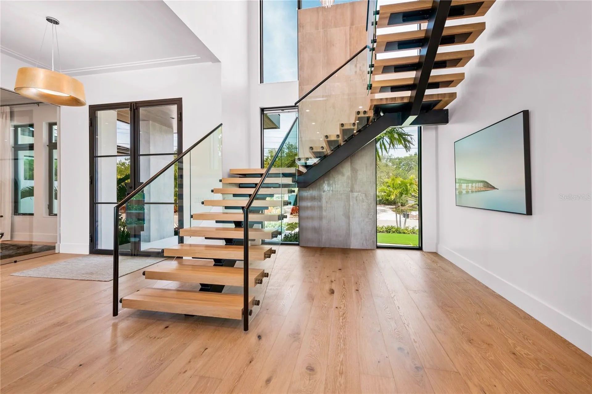 Modern open living room with floating wood staircase, glass railing, and large windows