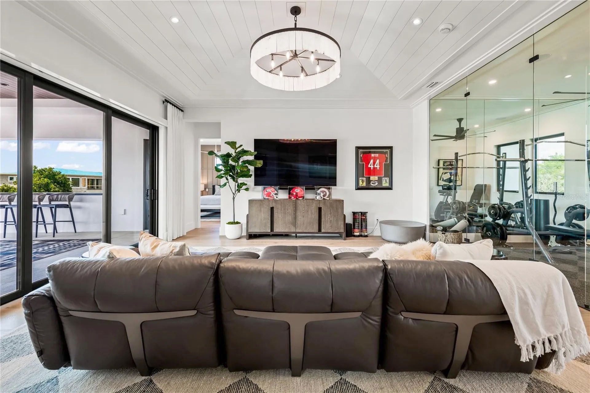 Modern living room with gray sectional, wall-mounted TV, fireplace, large windows, and glass sliding doors