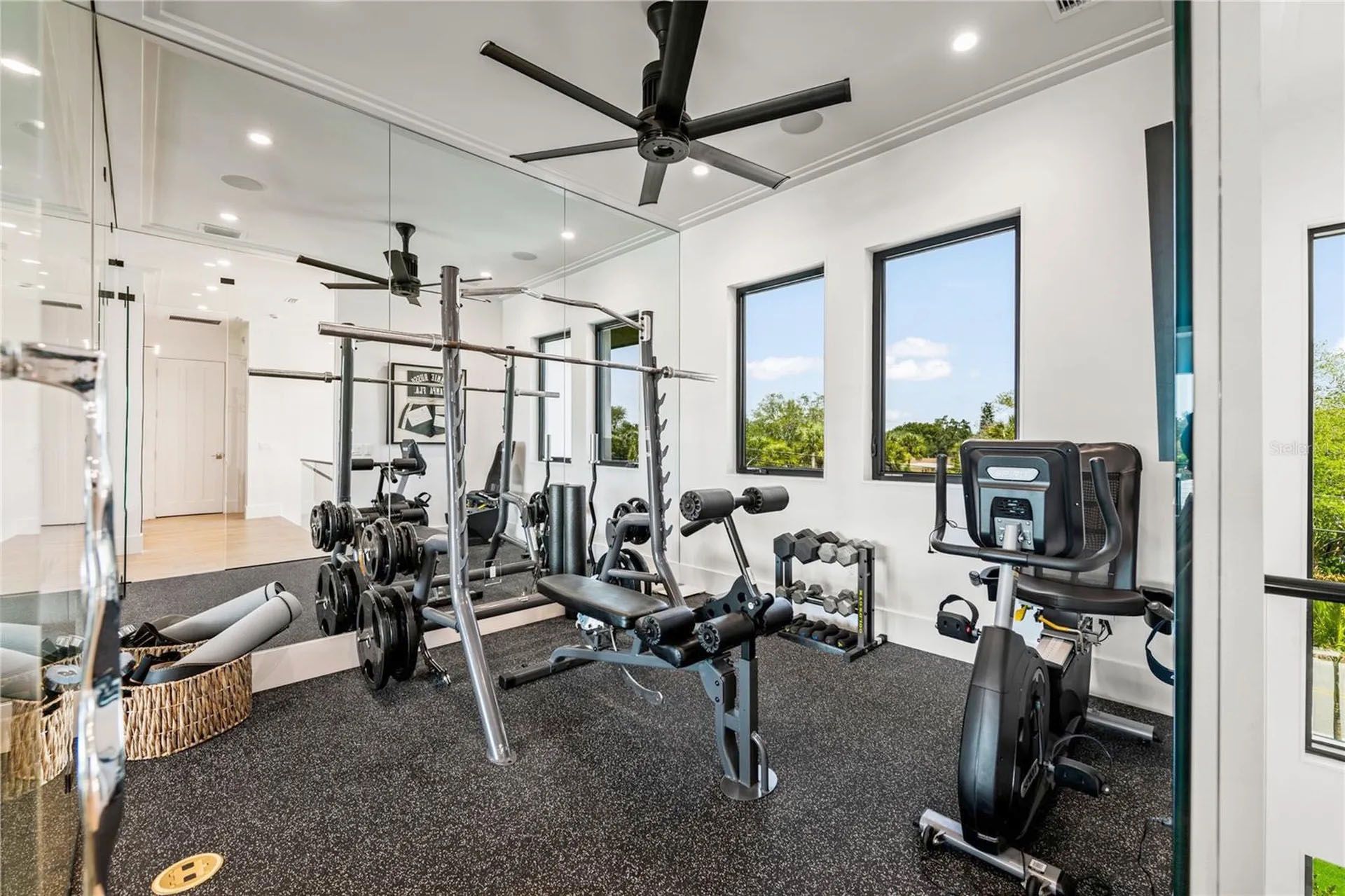 Modern home gym with weights, bench, cable machine, and large windows in a bright room