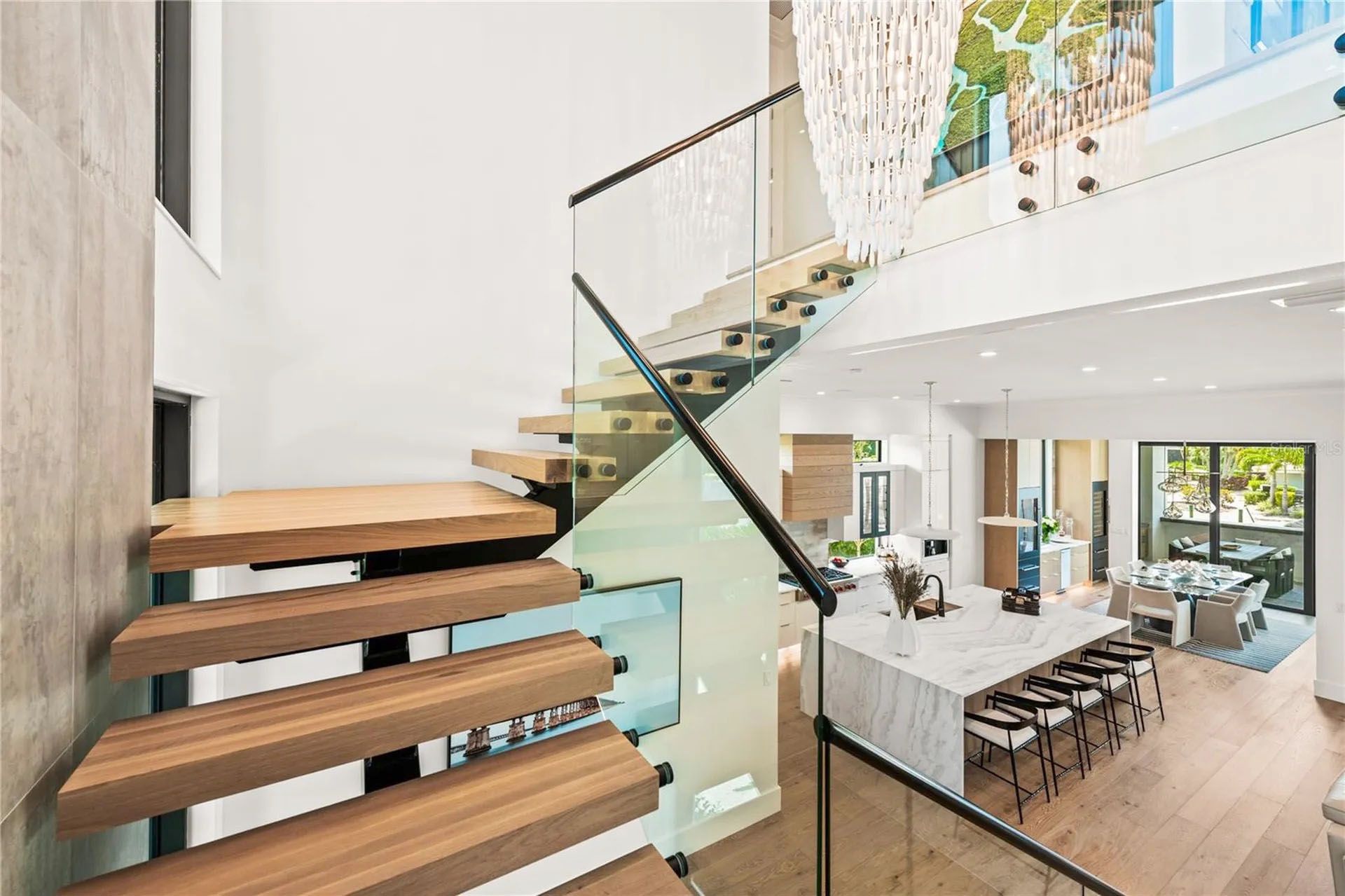 Modern home interior with floating wooden stairs, glass railing, and bright dining area below