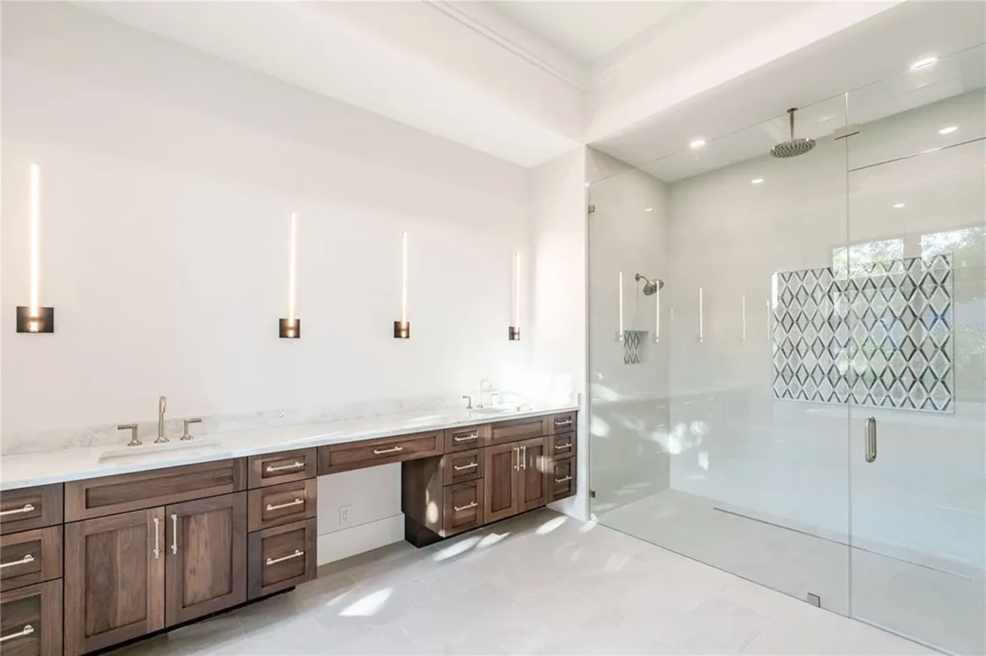 Bright modern bathroom with double vanity, dark wood cabinets, white walls, and glass shower