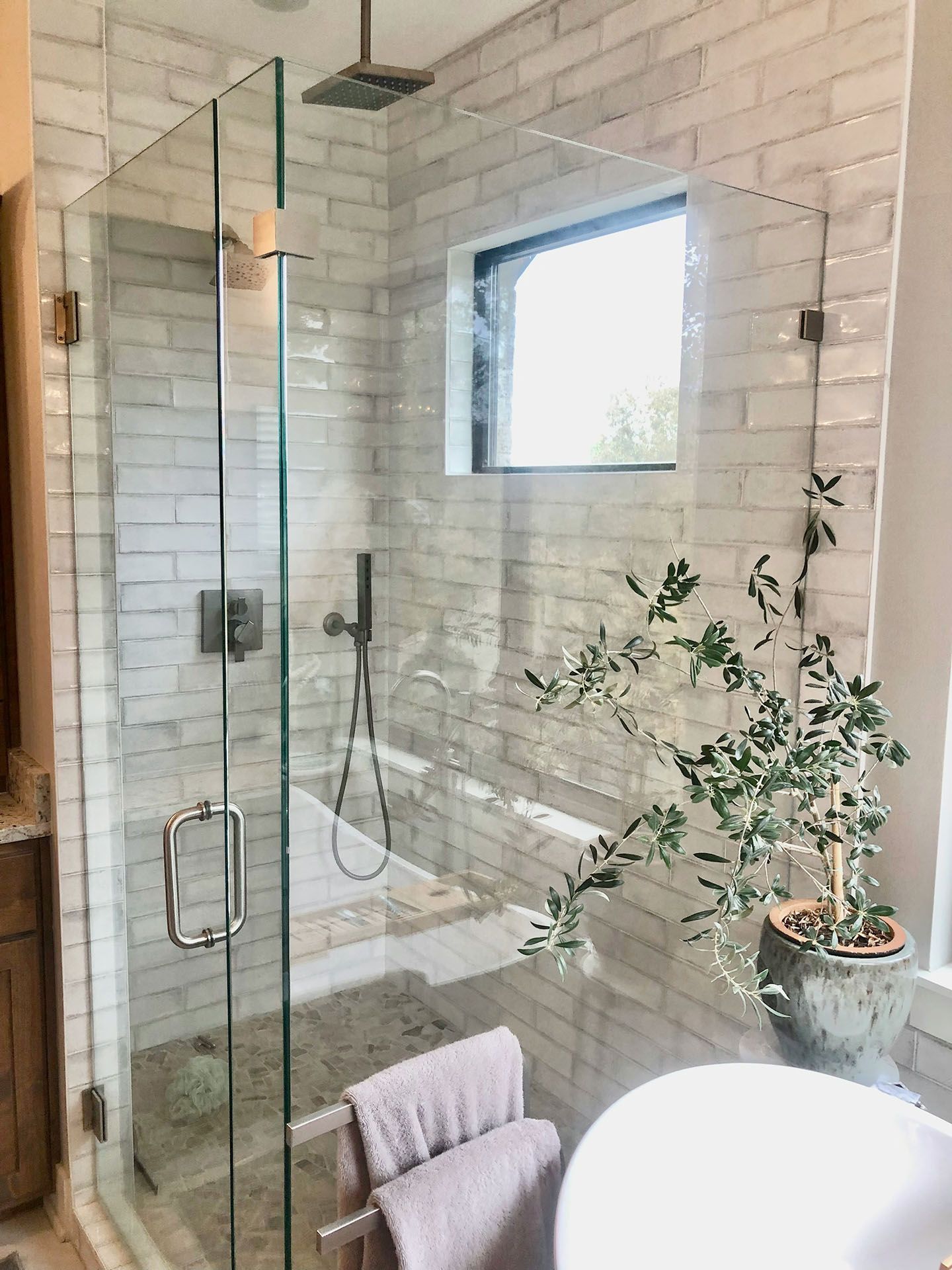 Modern bathroom shower with glass enclosure, white tile walls, window, and potted plant