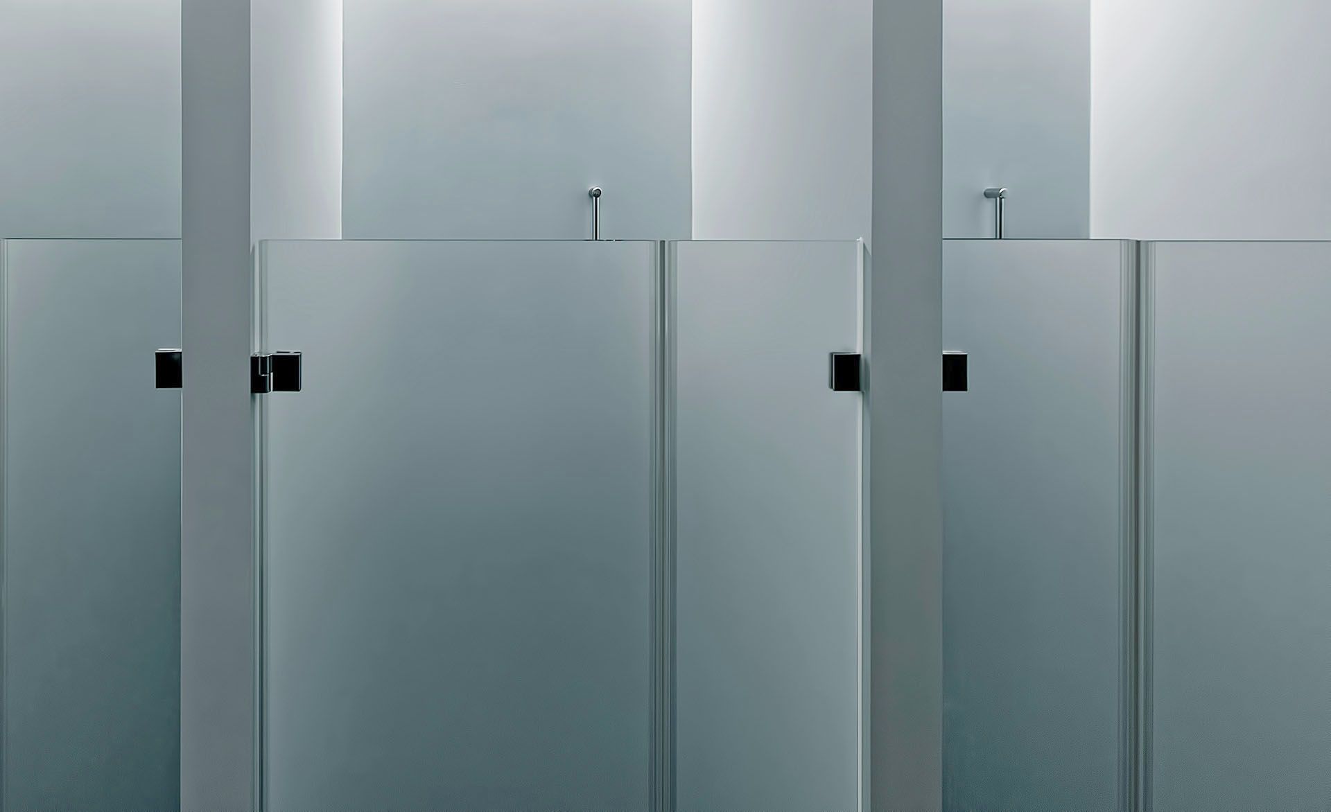 Frosted glass stalls with silver metal dividers and locks in a modern restroom
