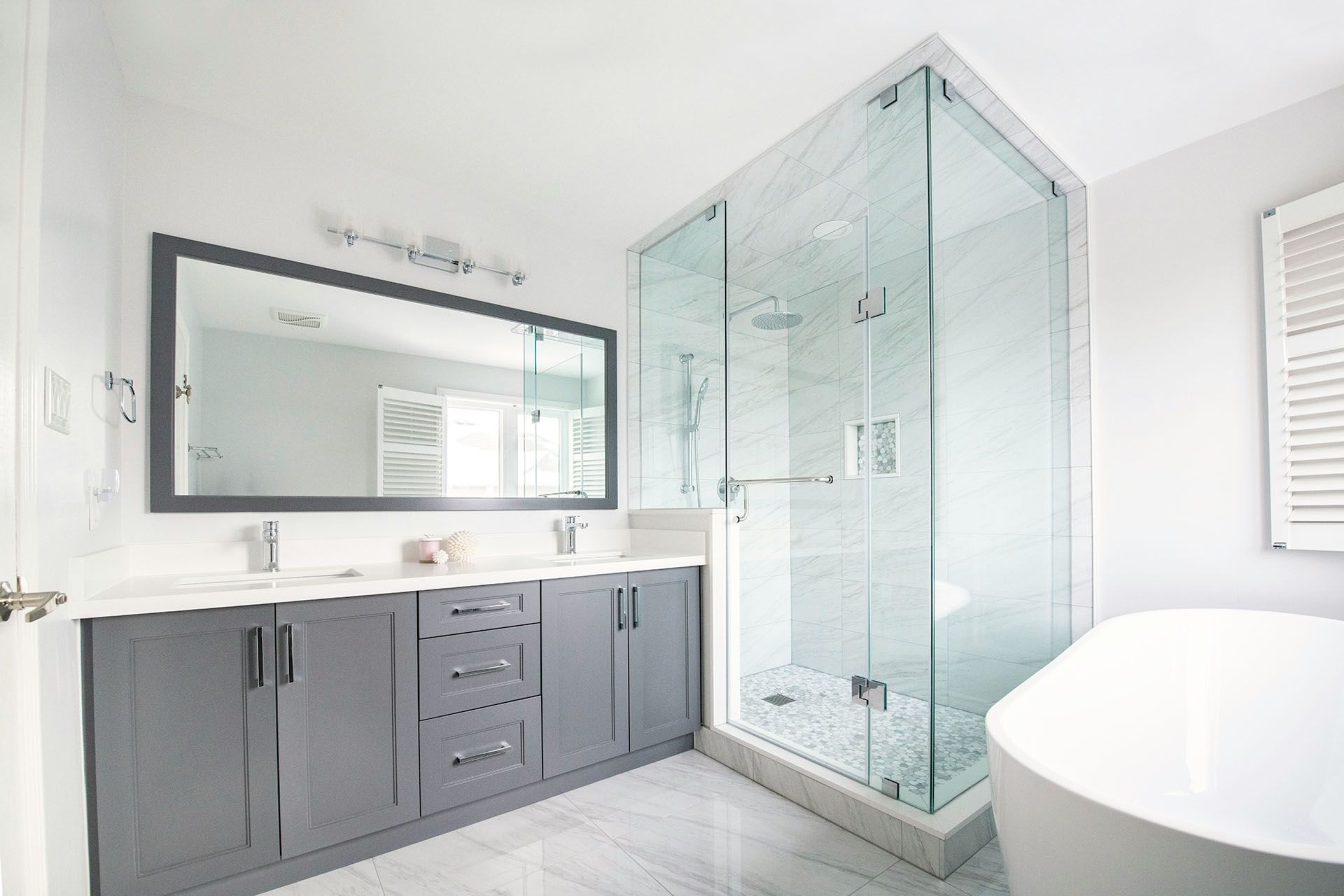 Modern bathroom with double vanity, large mirror, glass shower, and white tub