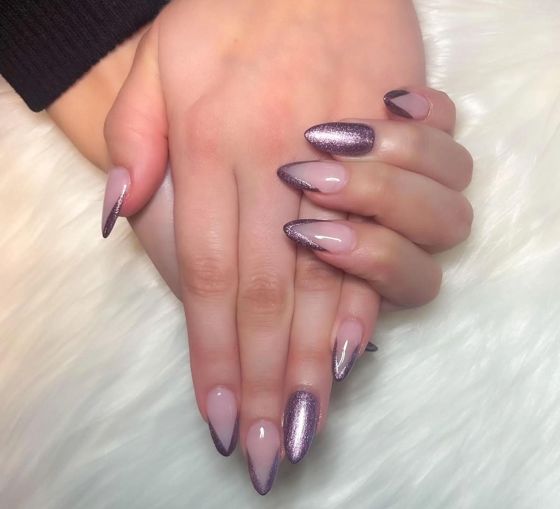 Hands with long, almond-shaped nails.  Some nails have glitter tips, others have a thin silver outline.  The nails are on a white, fluffy surface.