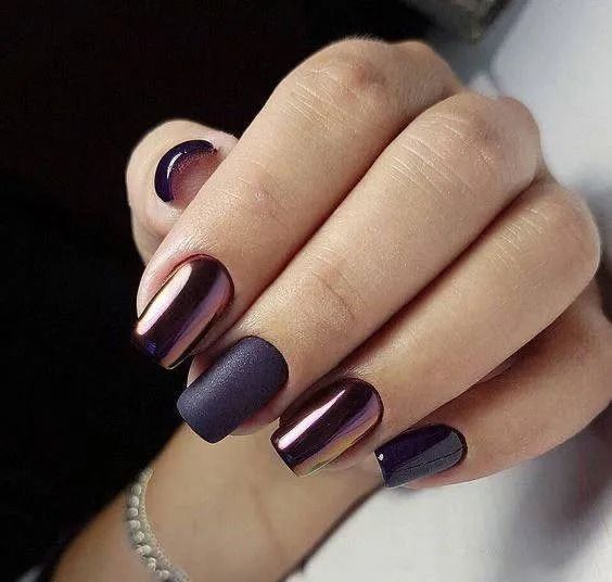 Hand with dark purple nails, some matte, some chrome, against a plain background.