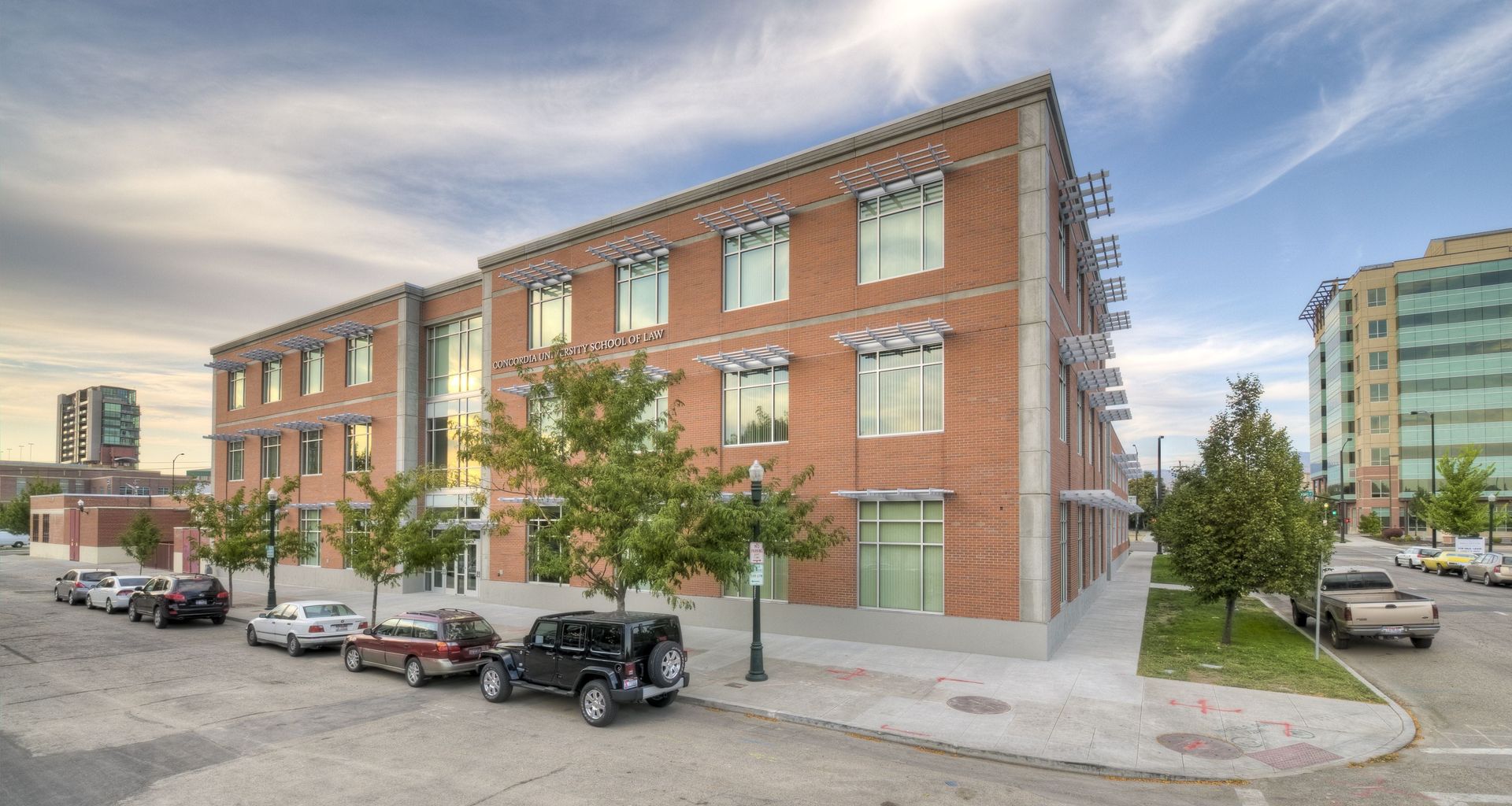 Red brick building with awnings, trees, parked cars, and a blue sky.