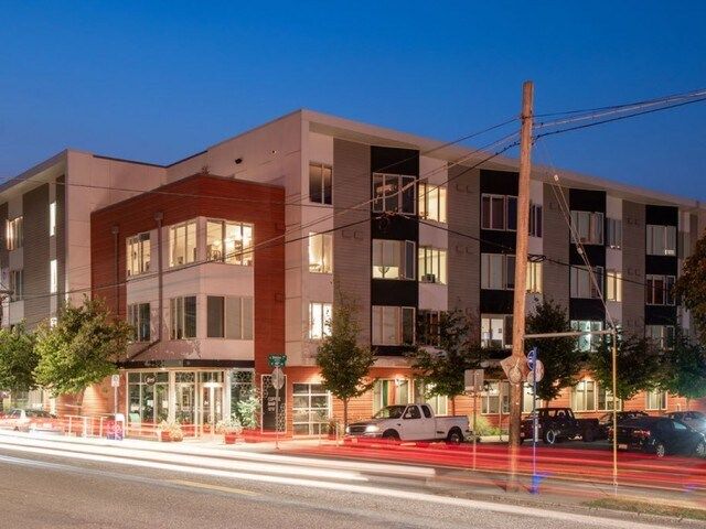 Modern apartment building exterior at dusk, with street lights and cars.