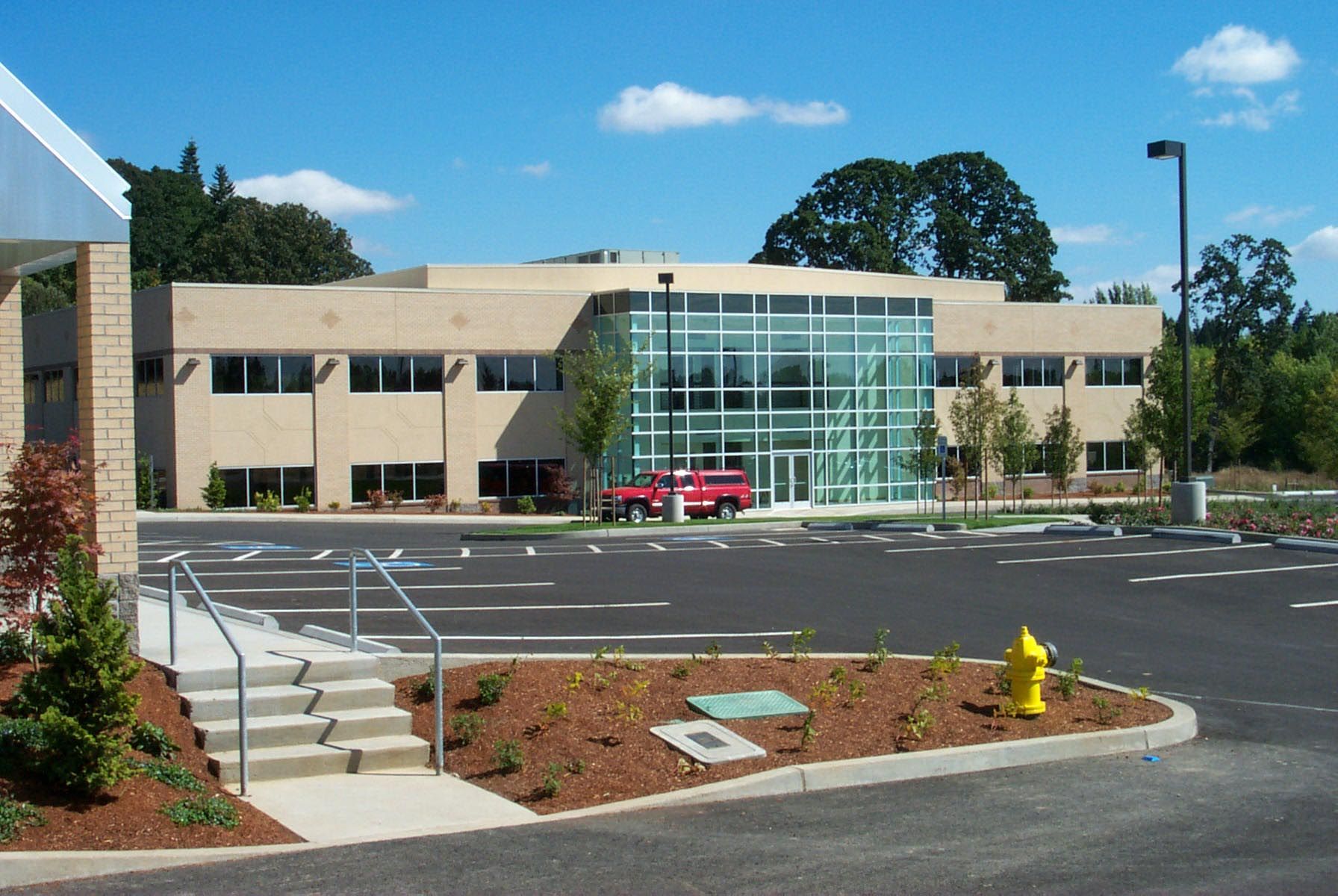 Modern building with glass entrance, tan walls, red truck, and parking lot under a blue sky.