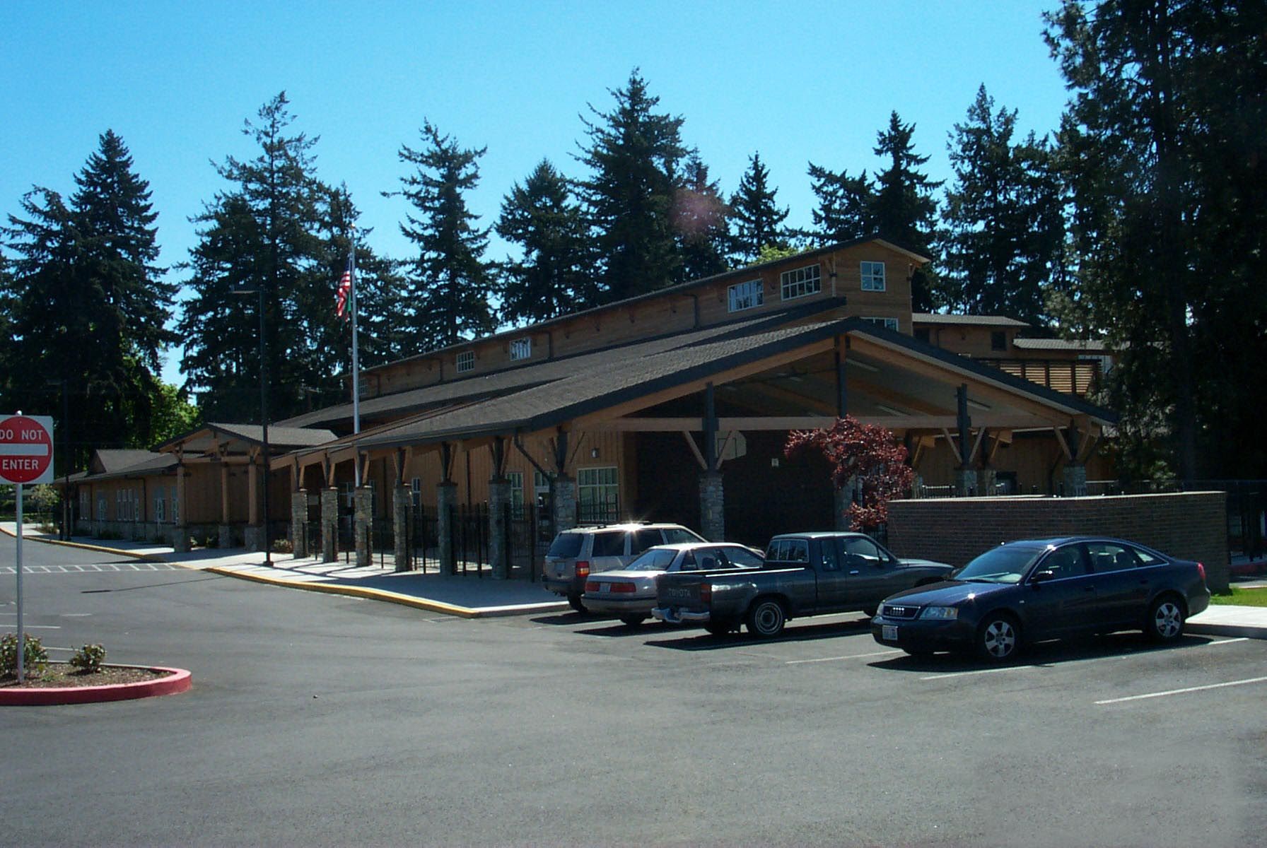 A single-story, wood-paneled building with cars parked in front; trees and a stop sign are in view.