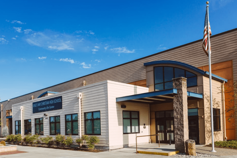 Exterior of a school building with a blue awning, American flag, and blue sky.