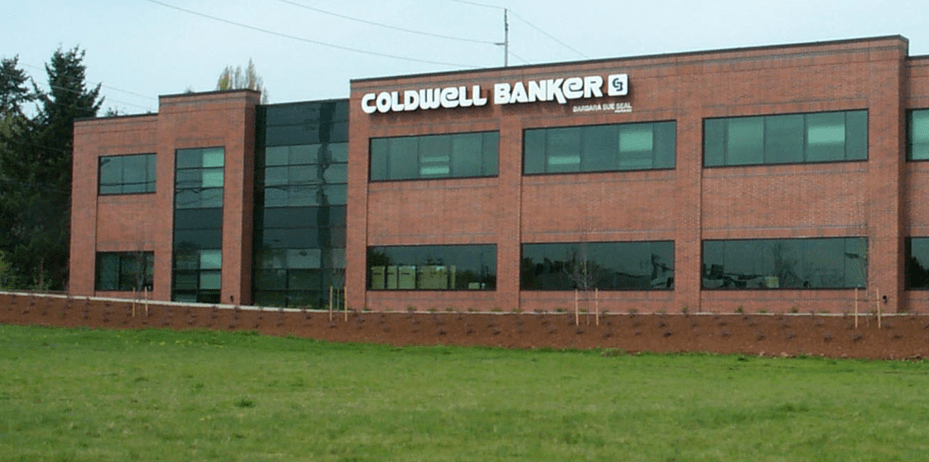 Coldwell Banker office building with red brick exterior and glass windows. Green lawn in front.