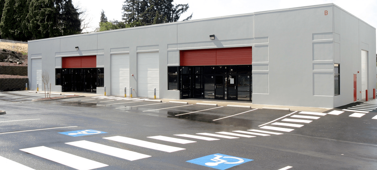 Exterior of a gray building with three garage bays; two bays have black contents, one bay has a white door, and a red overhead door.