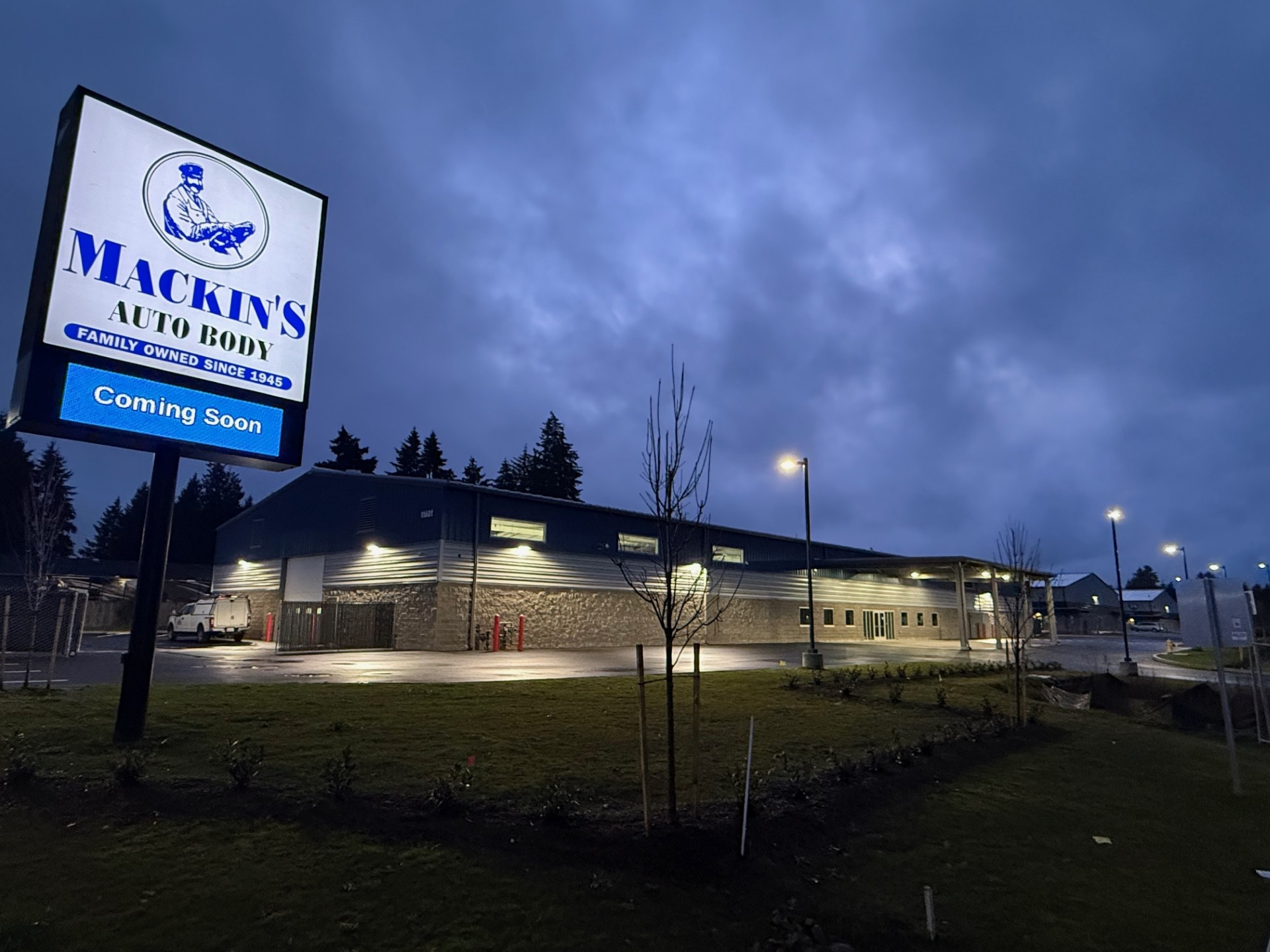 Mackin's Auto Body building at dusk, sign with logo. 