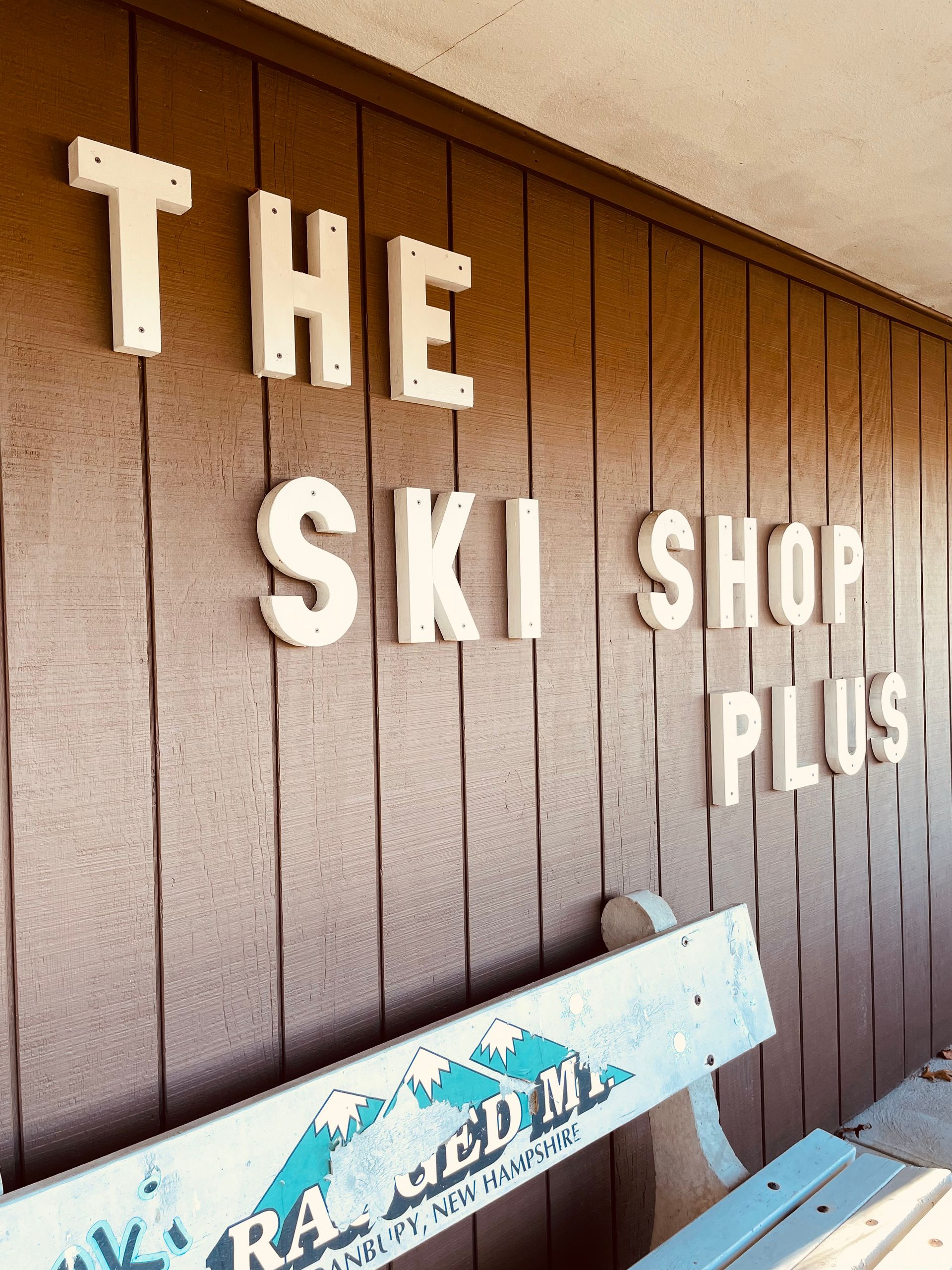 A sign for the ski shop plus is on a wooden wall