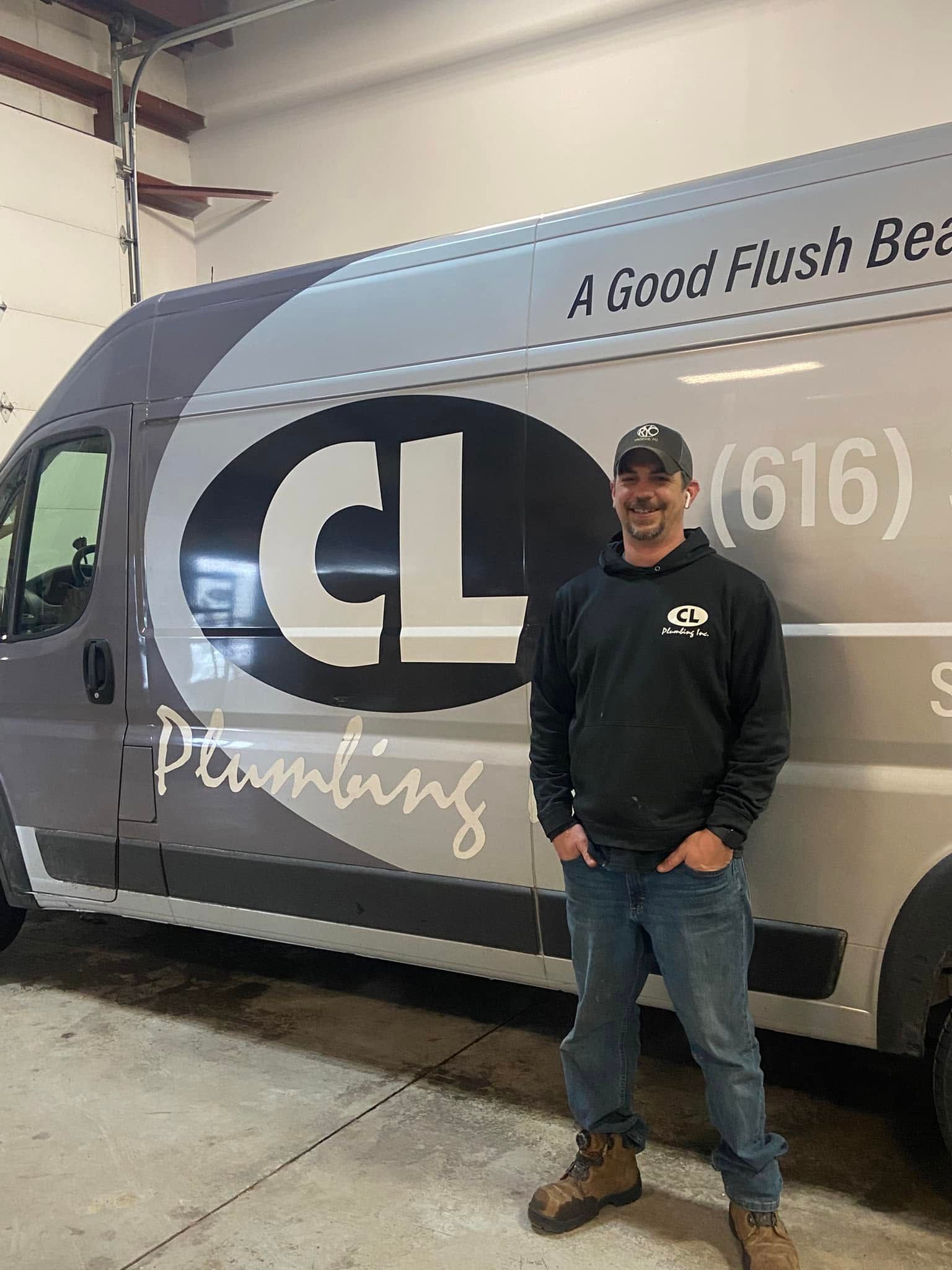 Man standing beside a gray service van with large “CL” logo in a garage.