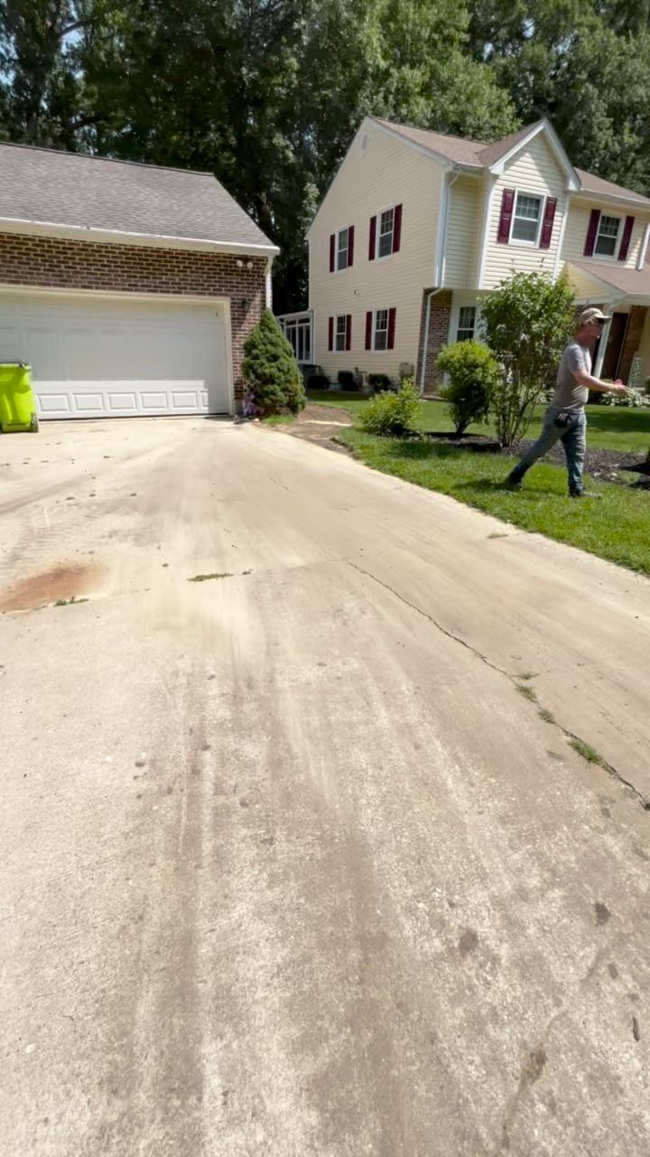 Driveway leading to a two-story beige house and a garage. A person is working on the lawn.