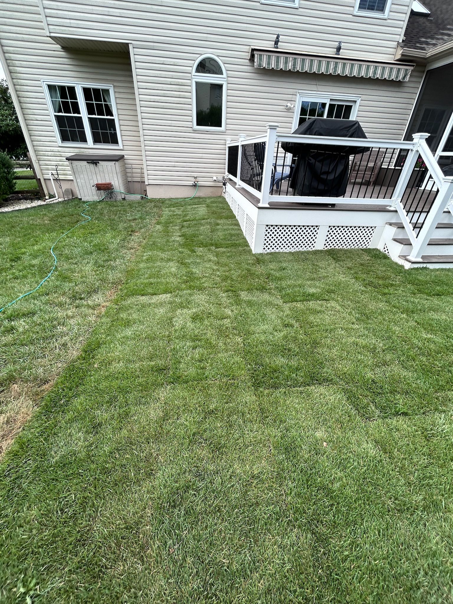 A beige house with white trim, a wooden deck, and a green lawn under a clear sky.
