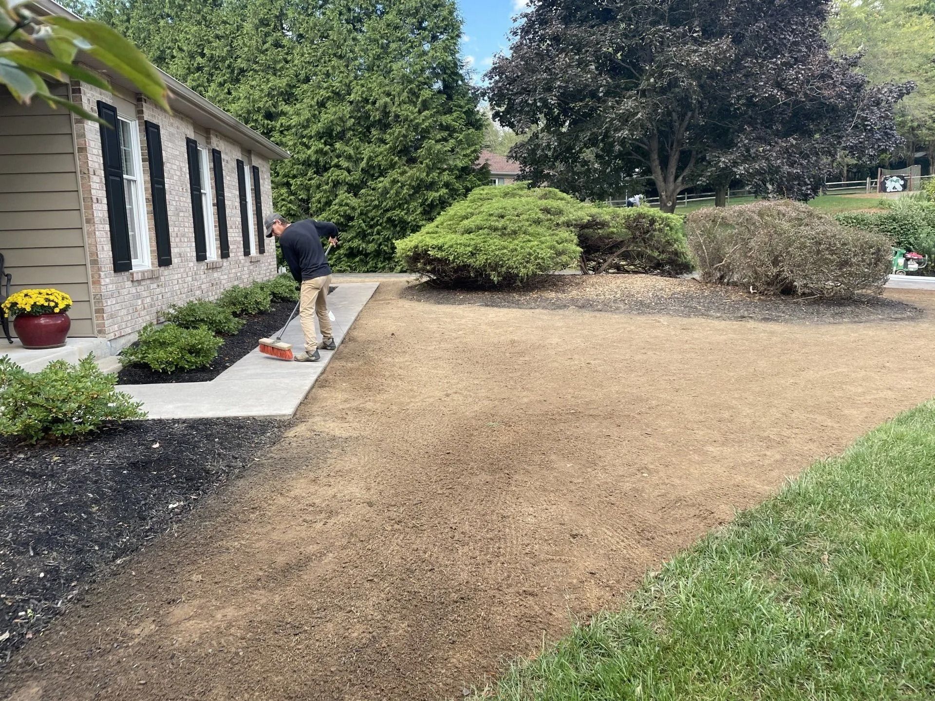 Man raking mulch on a prepared lawn near a house with landscaping; sunny day.