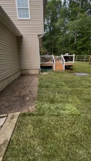Backyard with deck, lawn, and house. Beige siding, wooden deck, green grass, trees in background.