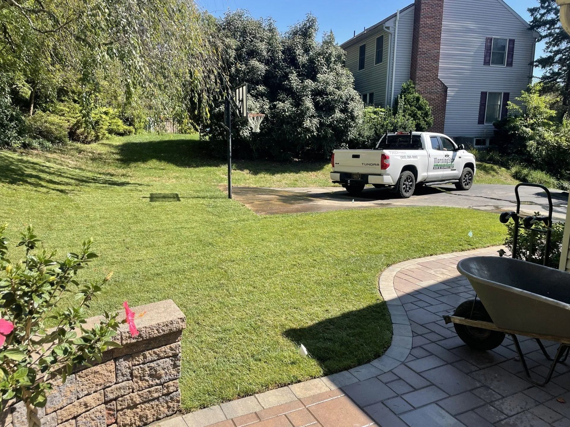 Green lawn with a white truck, house in background, brick patio in foreground.