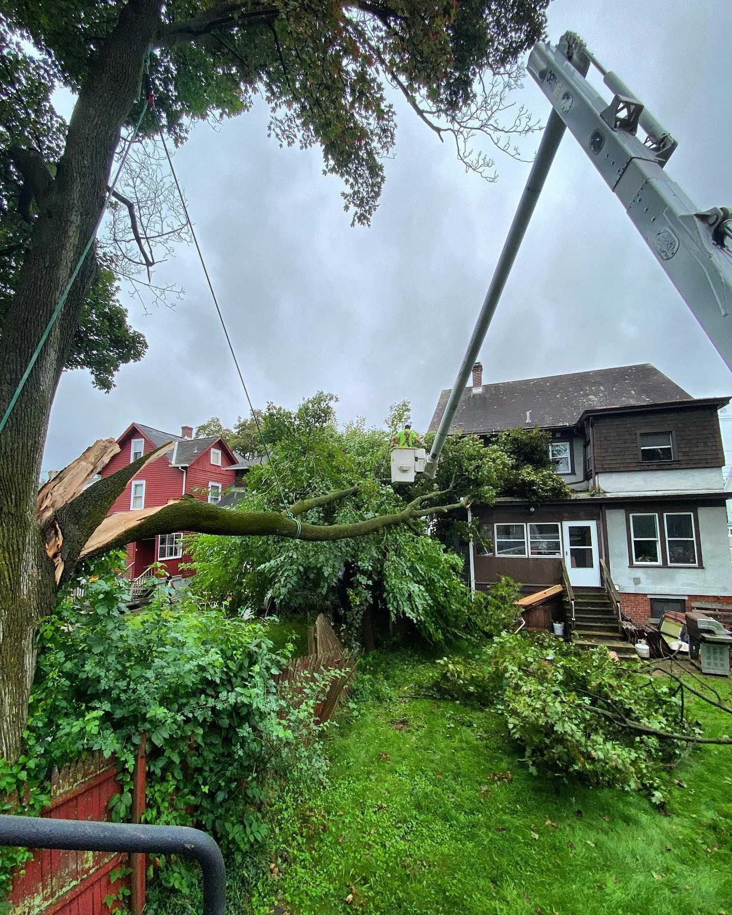 A bucket truck removes a large tree limb that has fallen onto the roof of a two-story house.