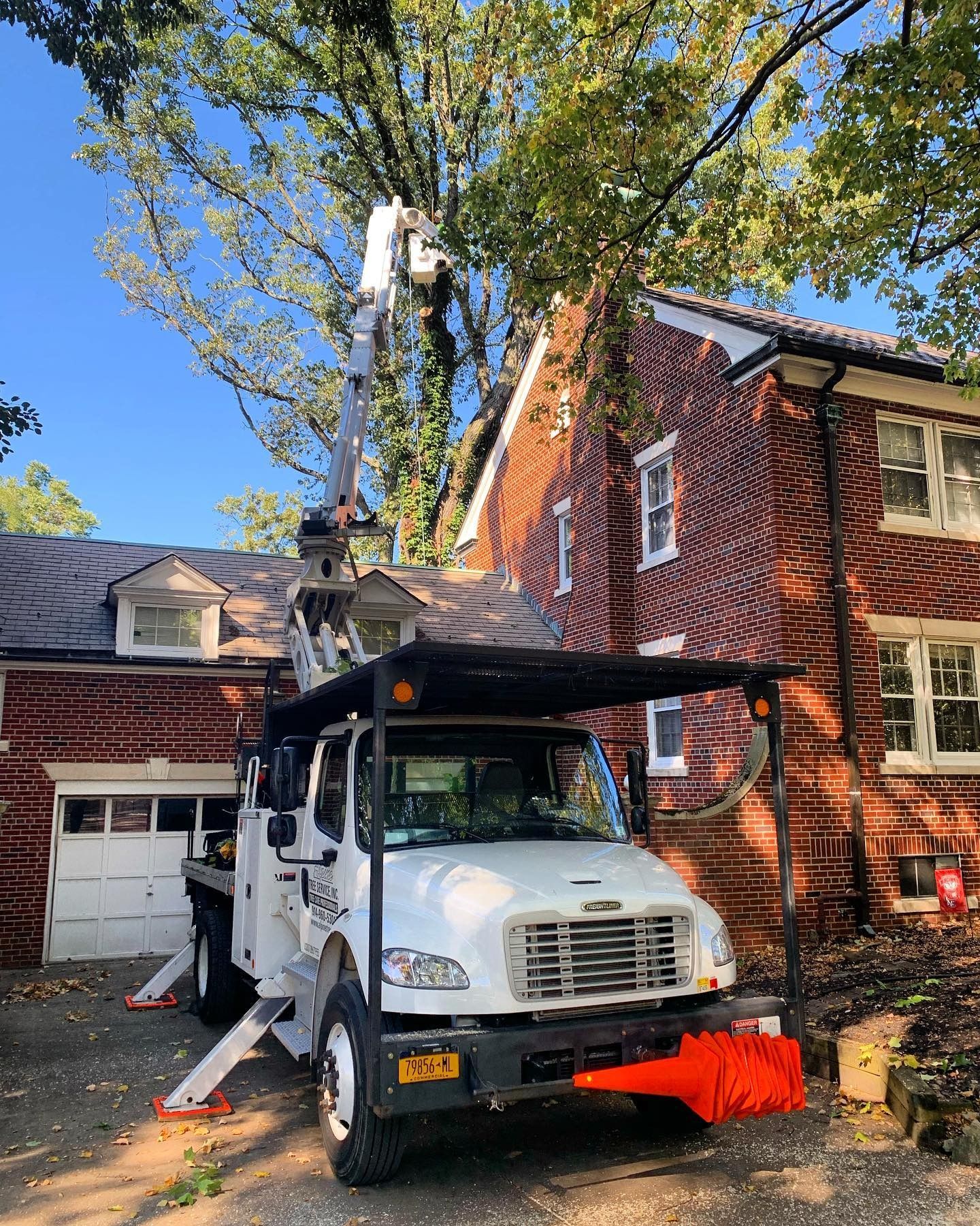 A white utility truck with an extended bucket lift parked in a driveway next to a brick house on a sunny day.