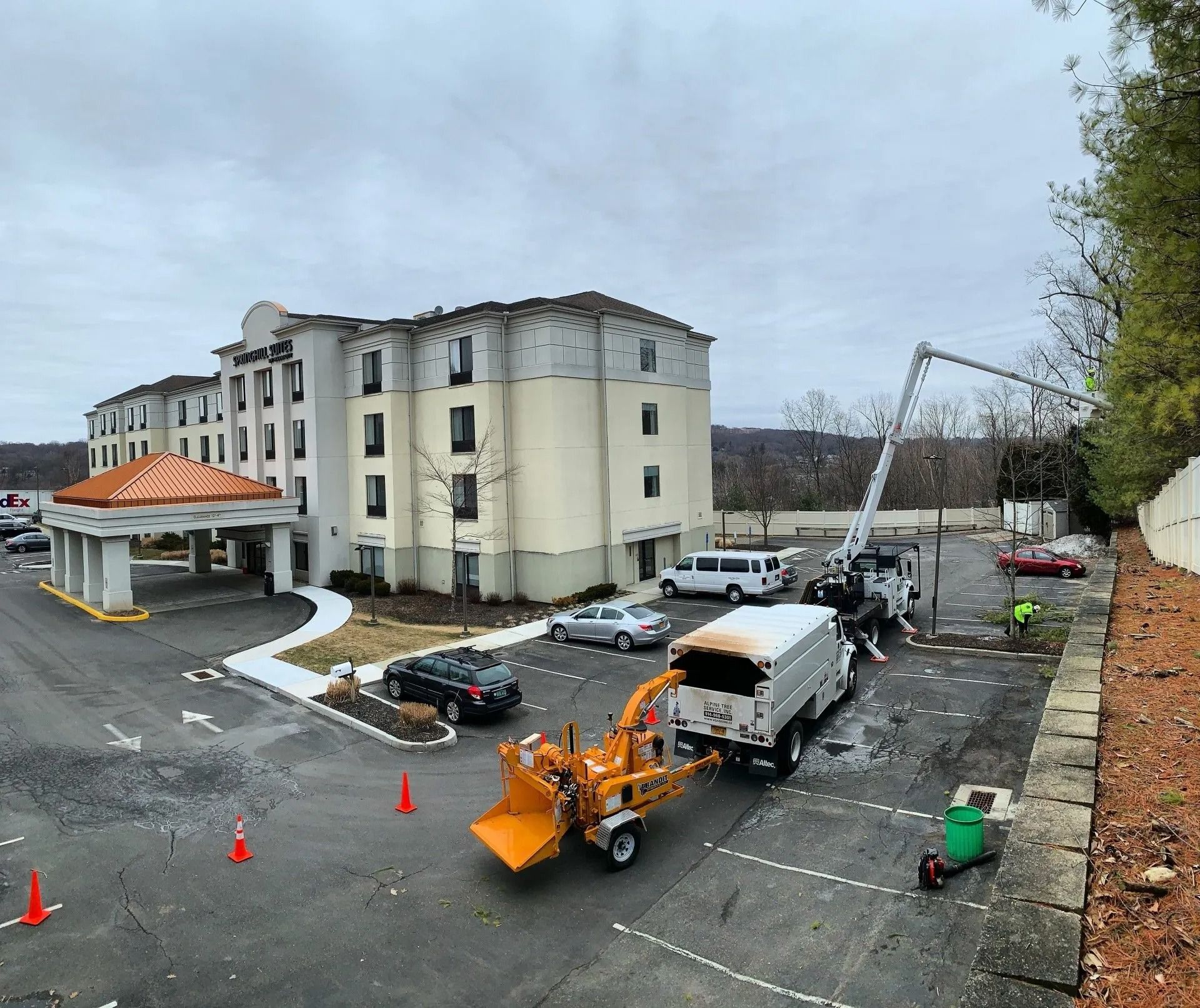 Tree maintenance equipment and a truck parked in the parking lot of a multi-story hotel on an overcast day.