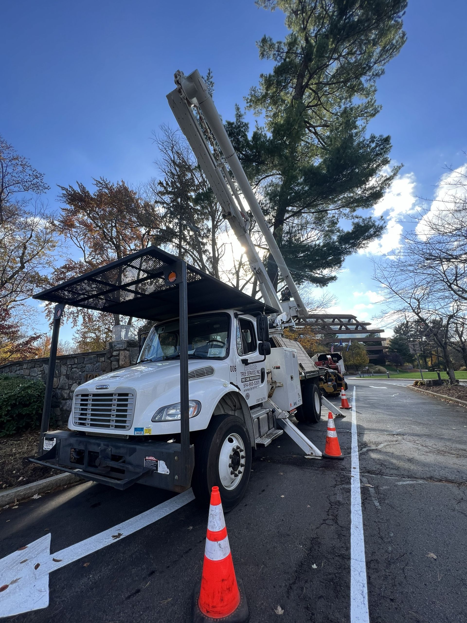 A white utility truck with an extended boom crane parked on a paved road, marked by orange traffic cones.