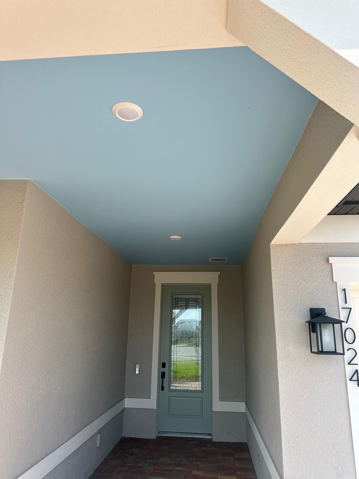 Front entry with a blue ceiling, a green door, and beige walls. A porch light and house numbers are visible.