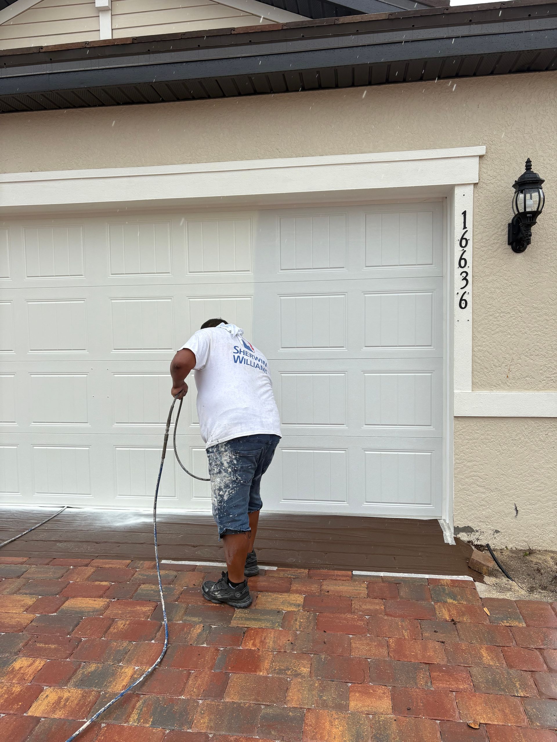 A person is painting a white garage door with a paint sprayer.