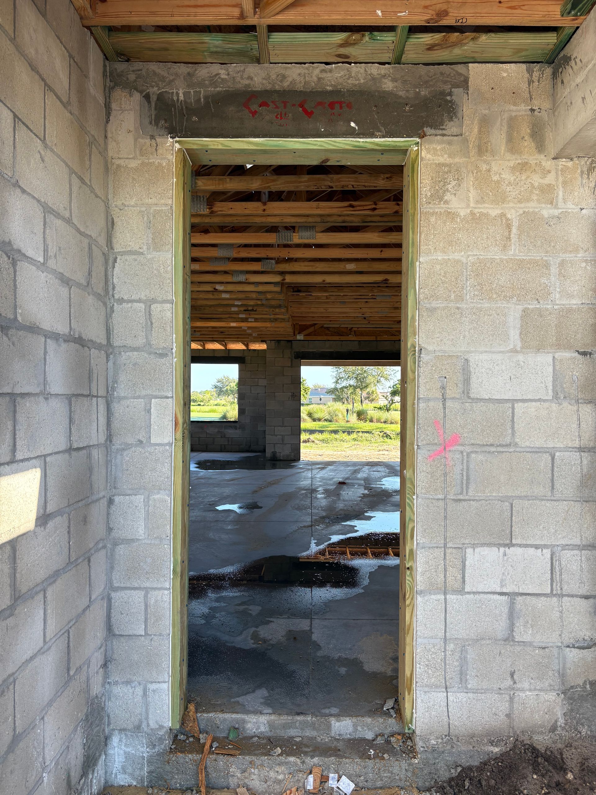View through a doorway in a concrete block building under construction. The doorway frame is edged with wood; the open doorway looks out on an unfinished interior.