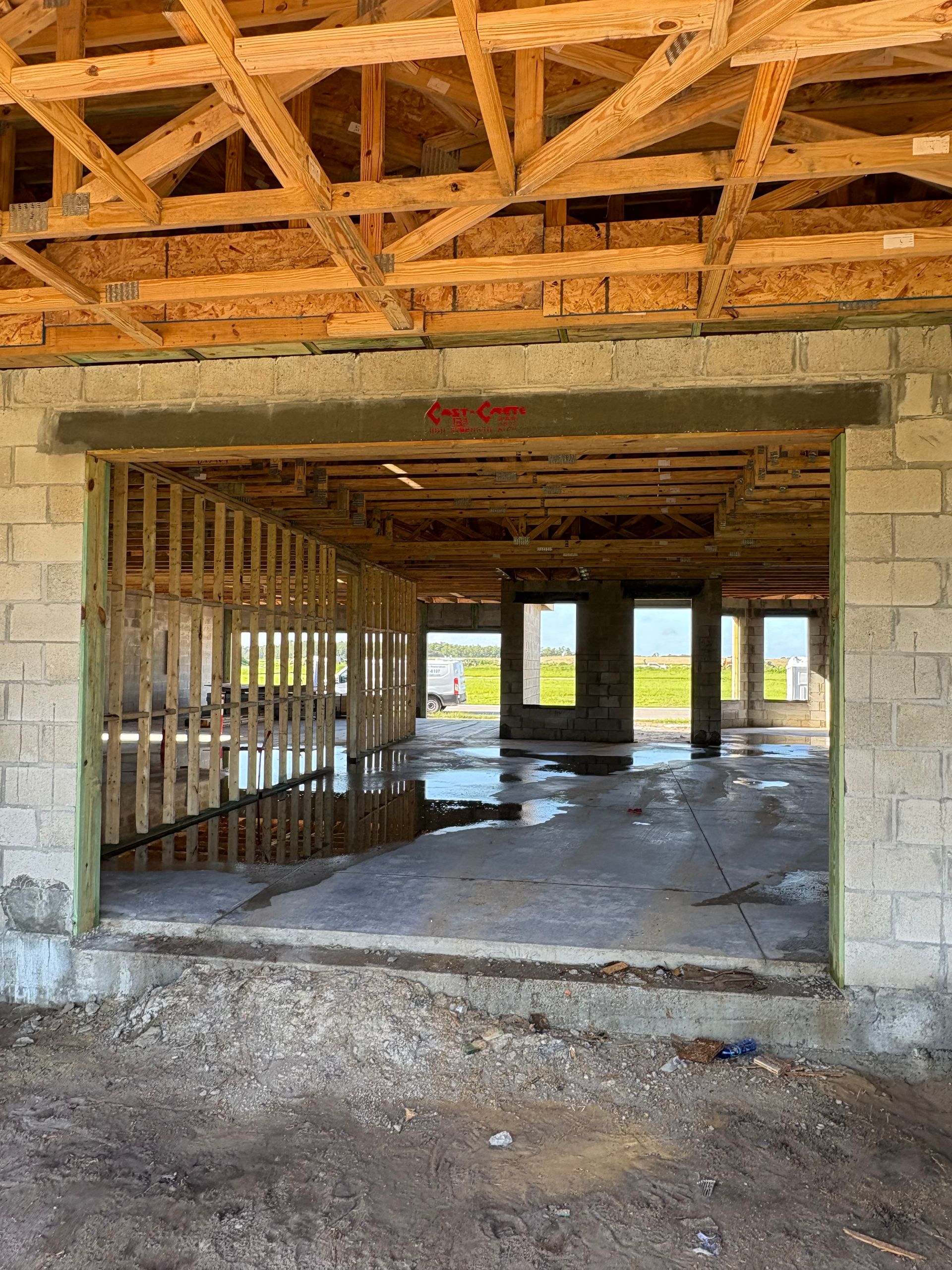 Construction site interior with unfinished walls and ceiling. A large doorway reveals framing and a partially flooded concrete floor.