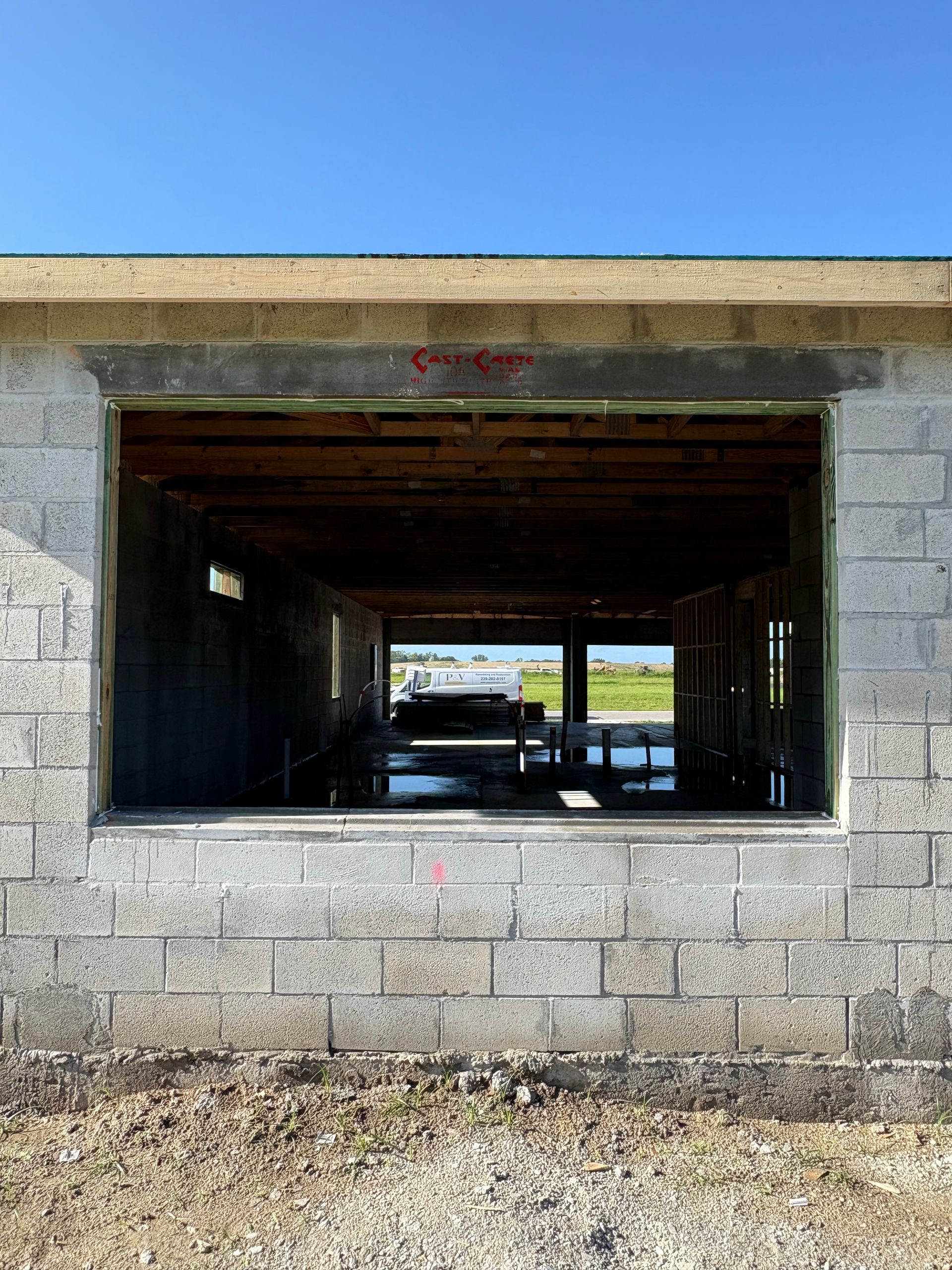 Exterior view of a cinder block building with an open window framing a view of water and land under a blue sky.