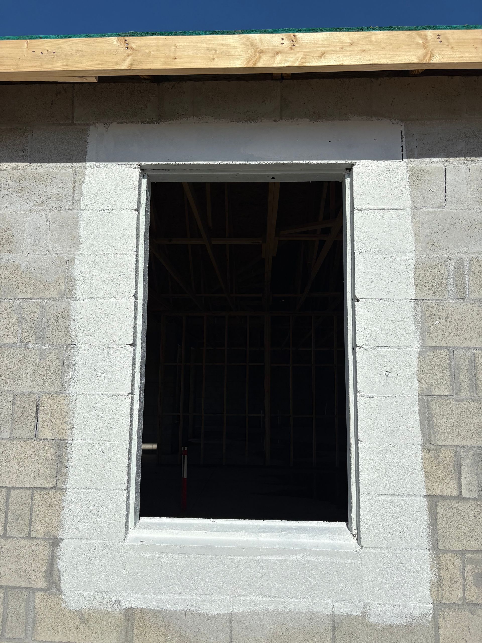 Construction site with a rectangular window opening framed by concrete blocks. The opening reveals the interior of a building with exposed framing.