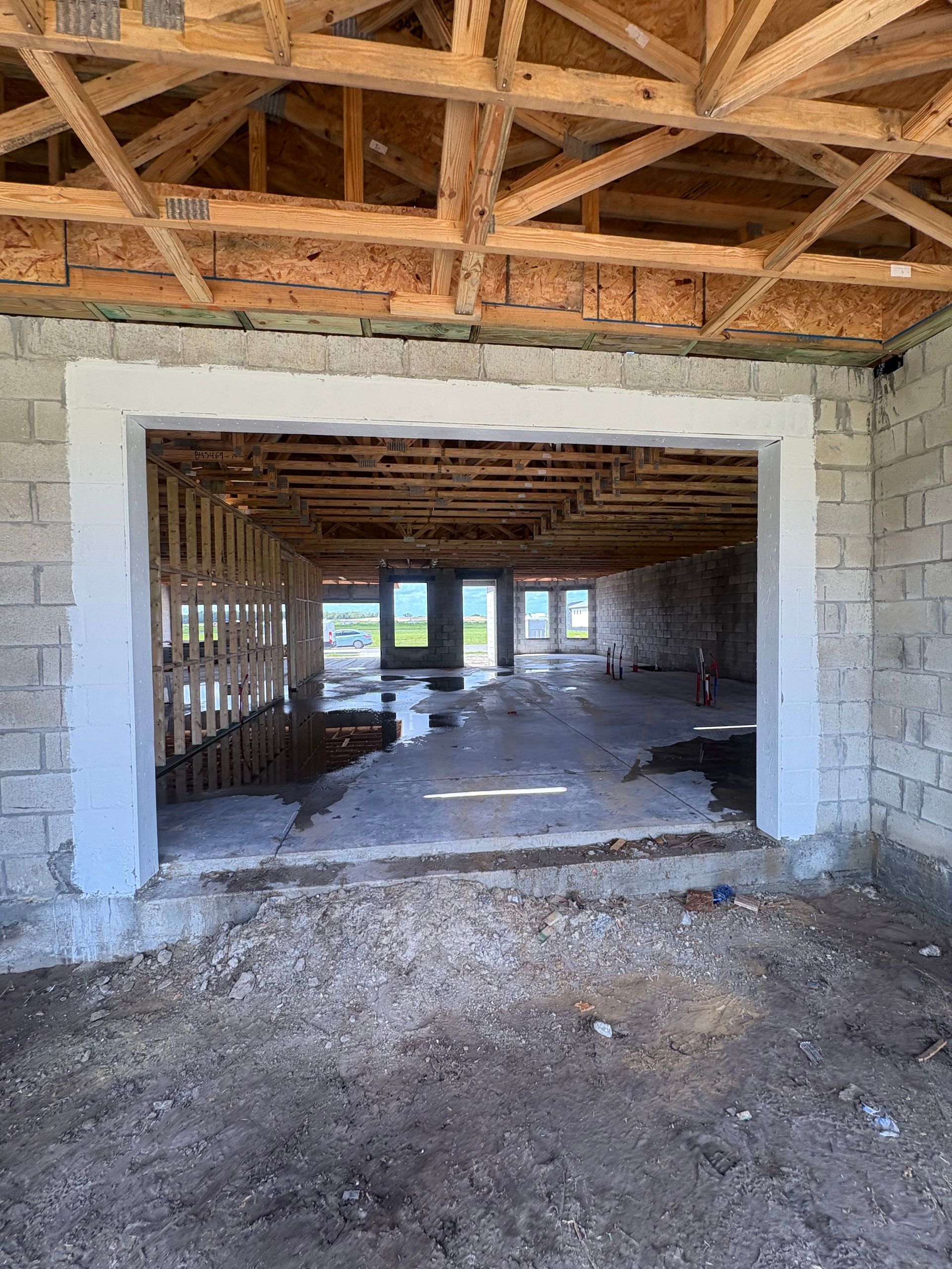 Interior of a building under construction, viewed through an open doorway. Gray cinder block walls surround an open floor with exposed wooden framing.