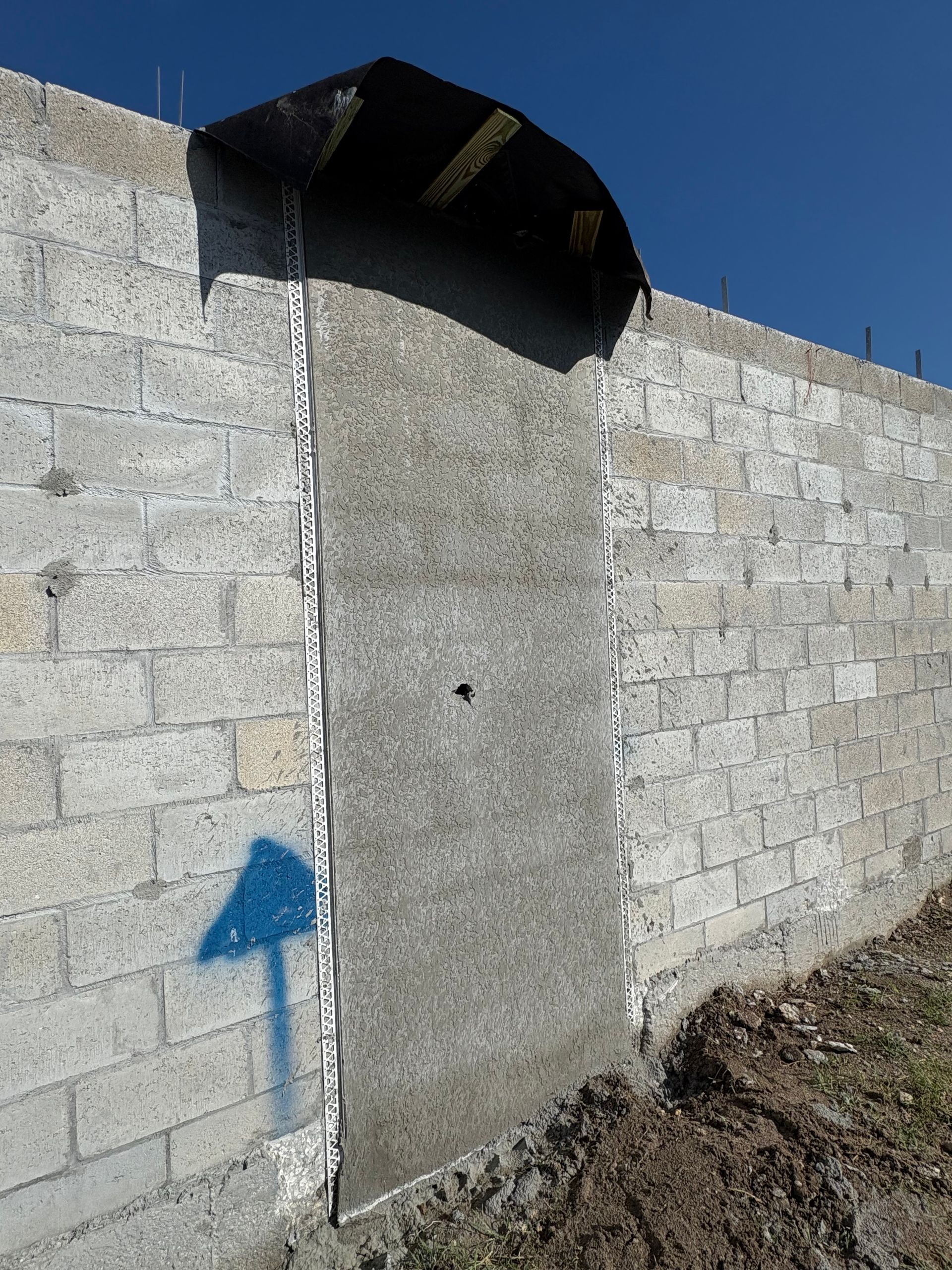 A concrete door-shaped patch set in a gray cinder block wall. A blue arrow points to the wall.