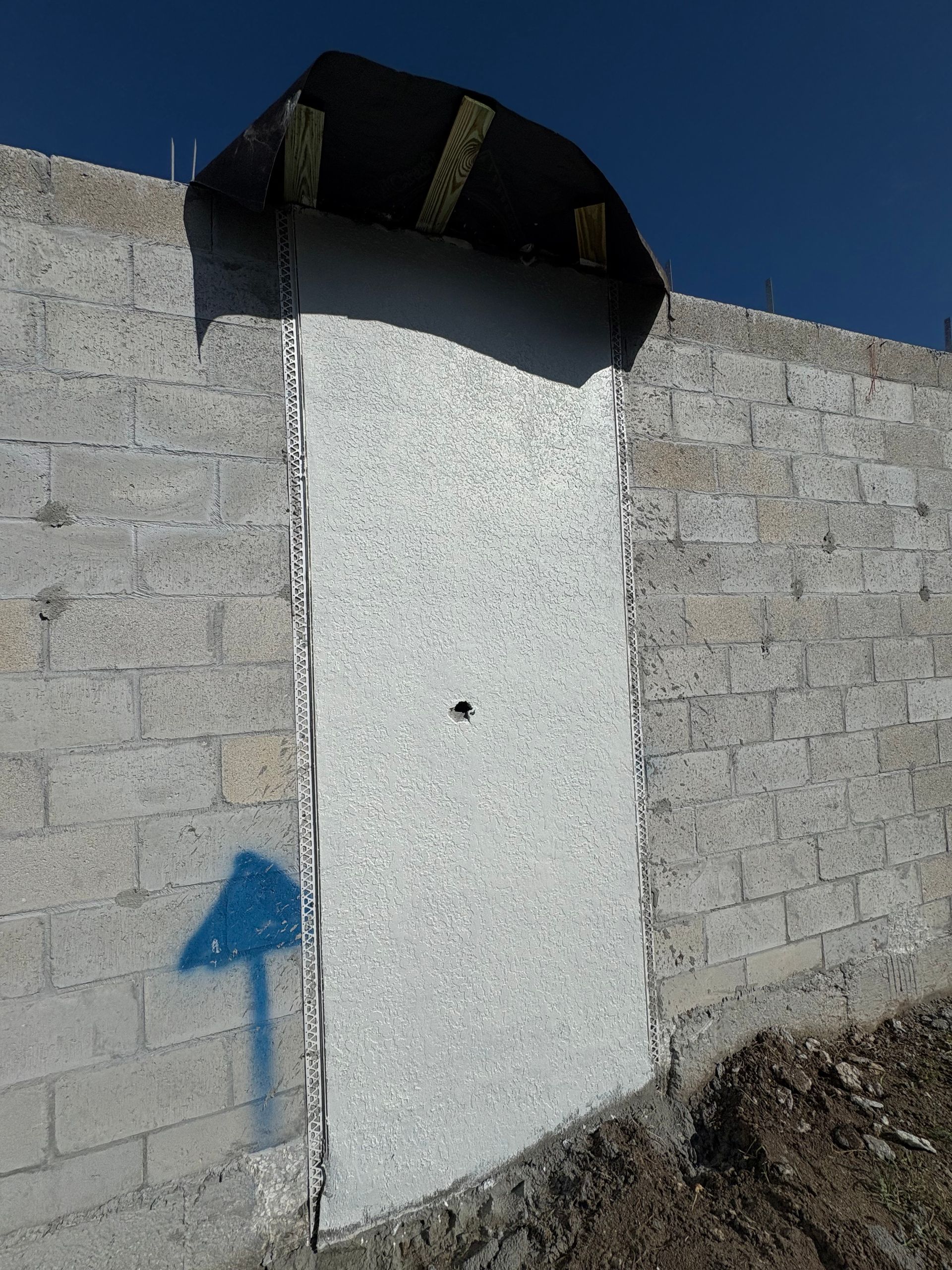 A boarded-up doorway in a concrete block wall with a blue arrow painted on the wall. The sky is clear blue.