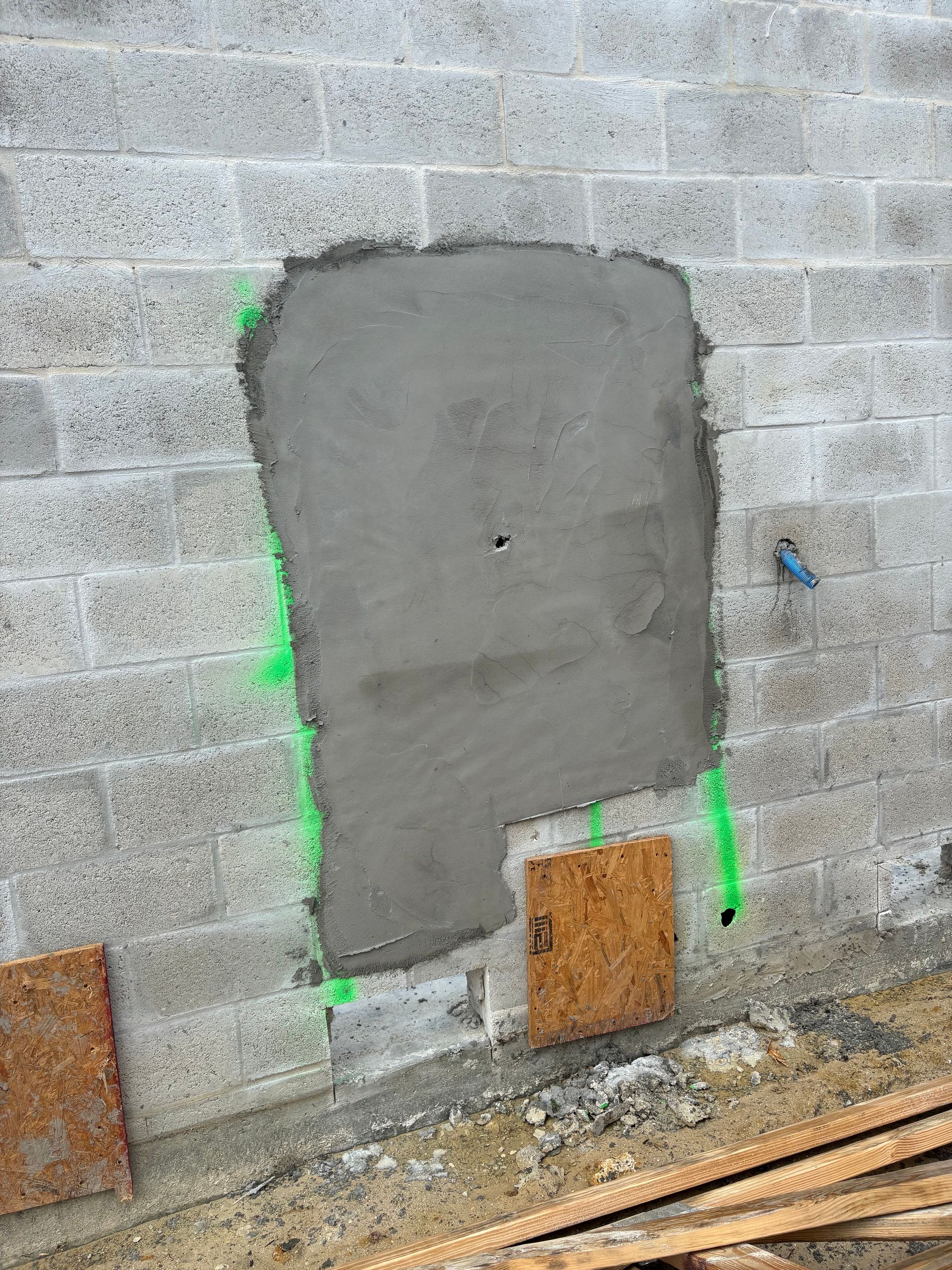 Patch of gray cement on a gray cinder block wall, possibly repairing an opening. Green spray paint outlines the patch.