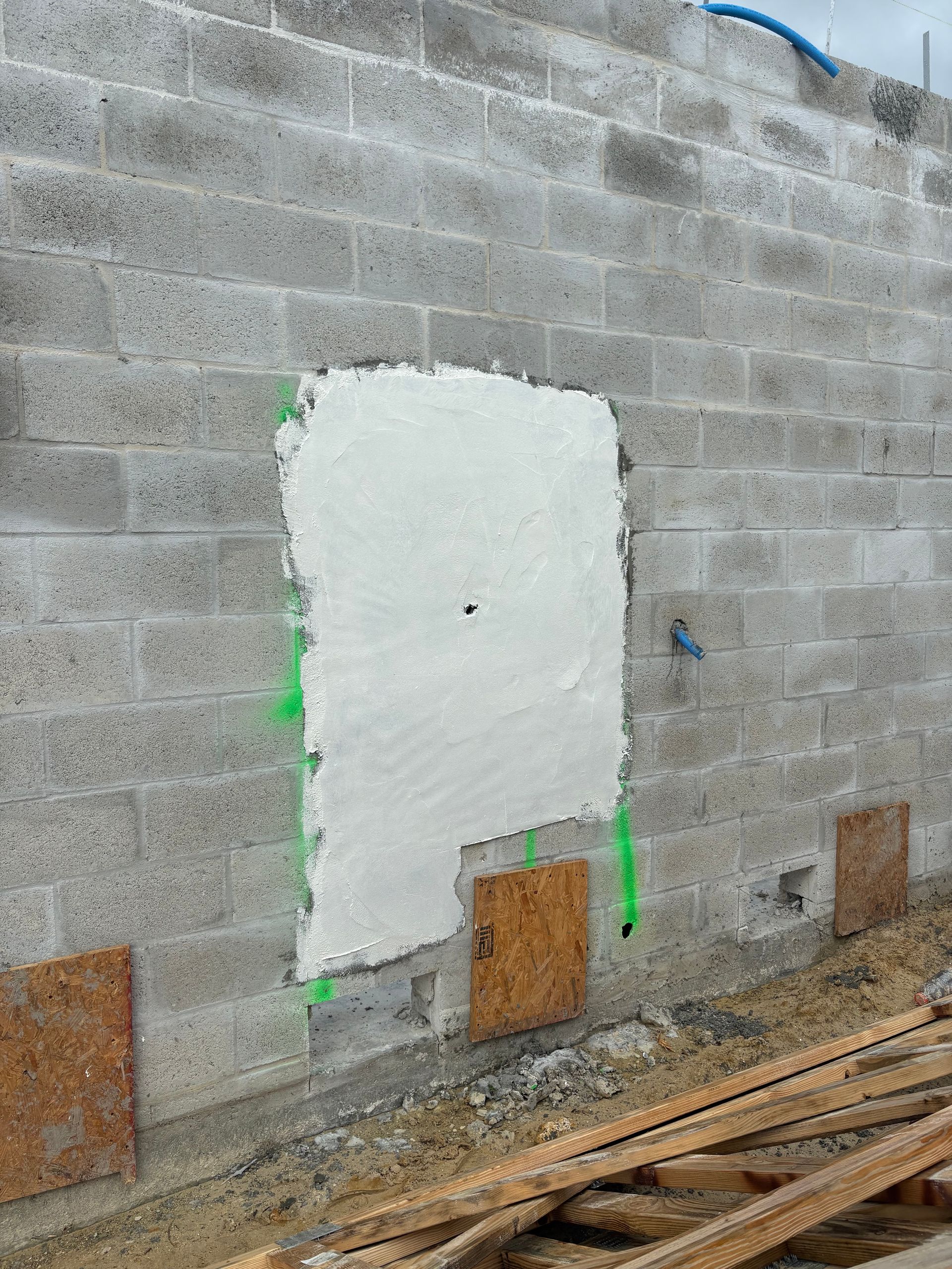 Gray cinder block wall with a rectangular white patch, possibly repaired. Wooden panels sit below.