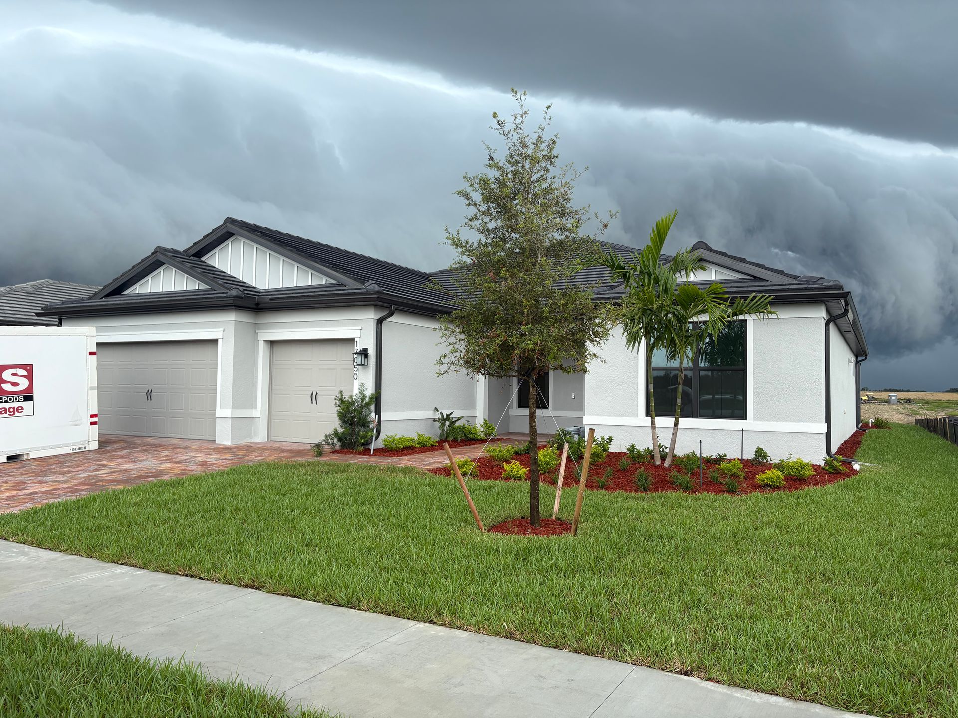 A house with a storm cloud overhead; green lawn, red mulch, and a gray garage face the storm.