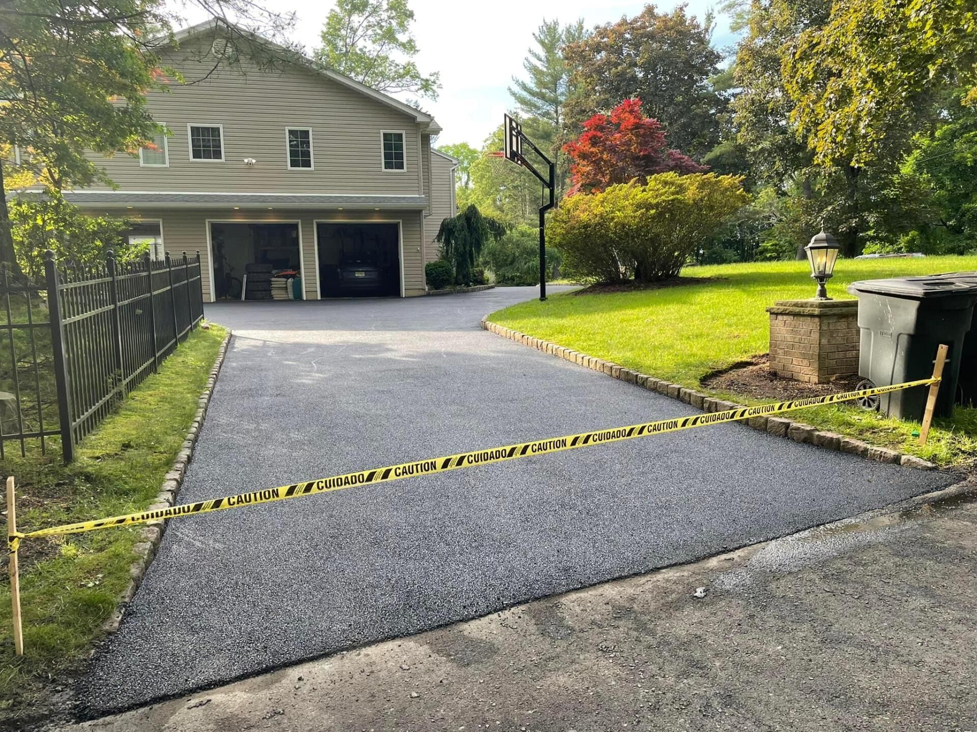 A newly paved asphalt driveway leads to a two-car garage at a suburban home, blocked off by yellow caution tape.
