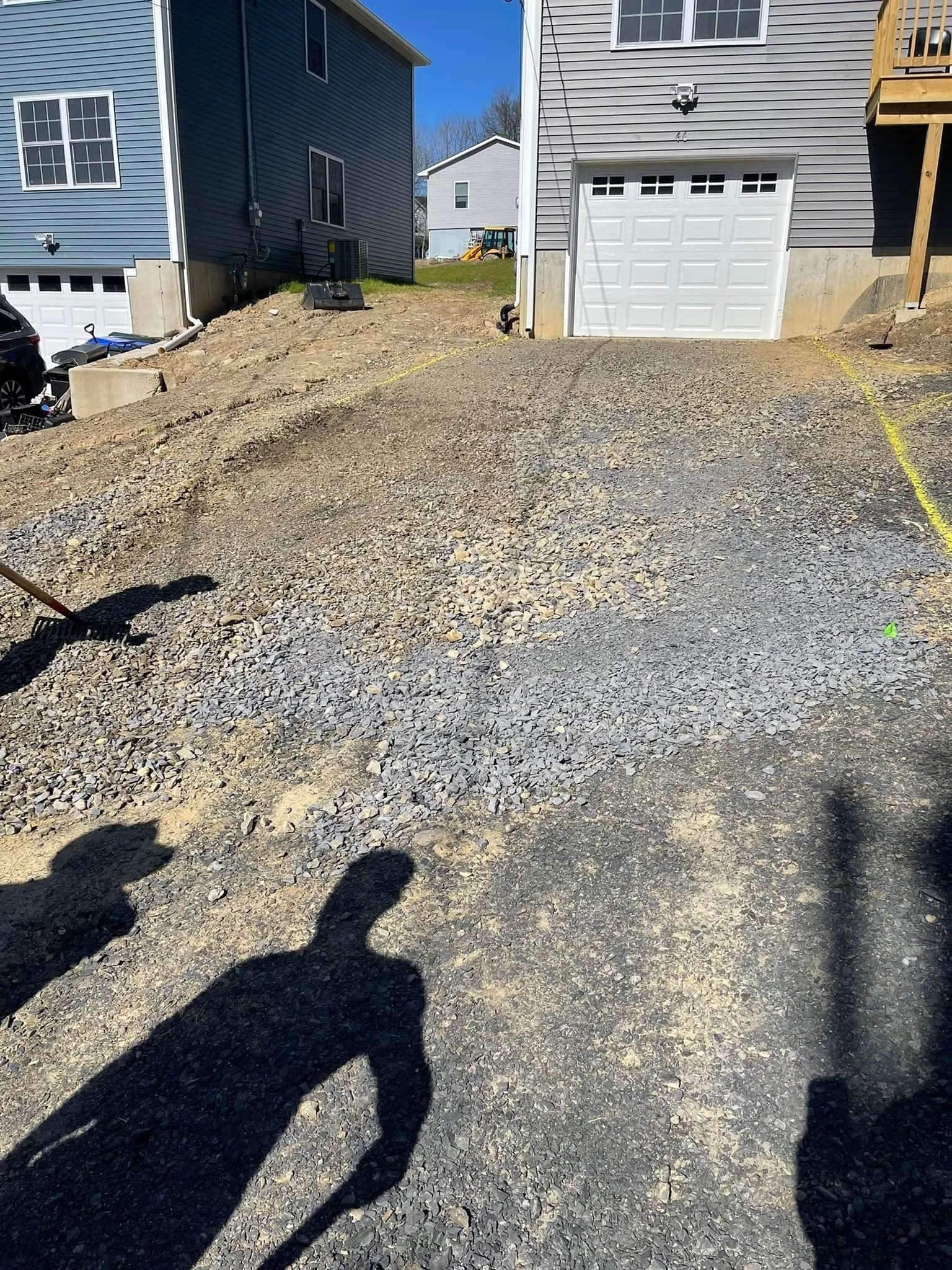 A freshly graveled residential driveway leading up to a two-car garage with long, human shadows cast in the foreground.