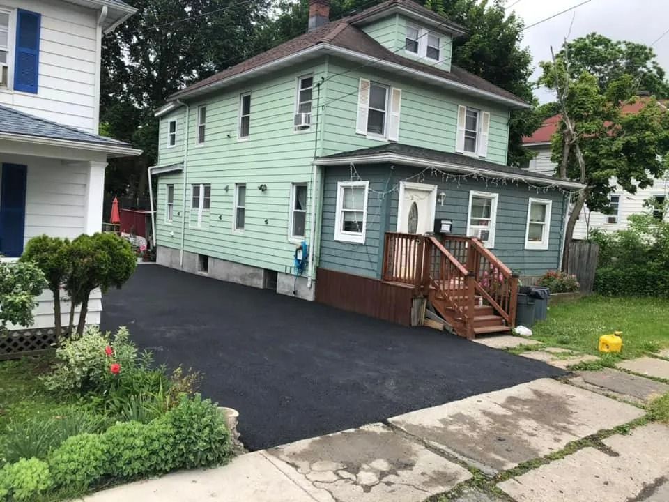 A green two-story house with a blue ground floor, wooden stairs, and a freshly paved black driveway.